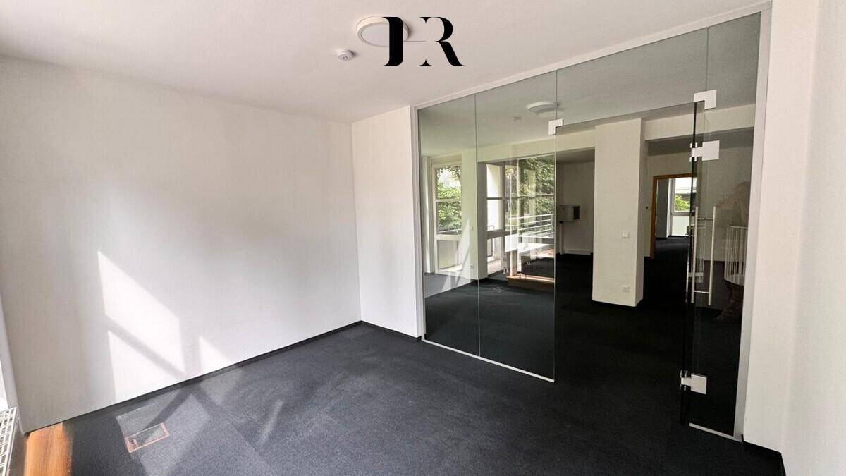 Moderner Büroraum mit Glaswänden, dunklem Teppichboden und viel Tageslicht.
