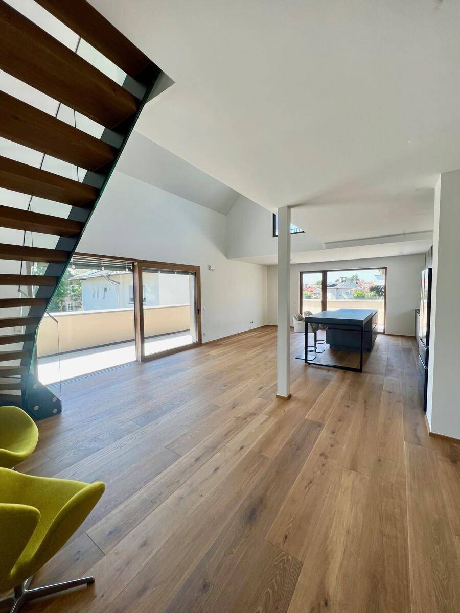 Großzügiger, offener Wohnbereich mit Holzboden, moderner Treppe und Zugang zu einem Balkon.