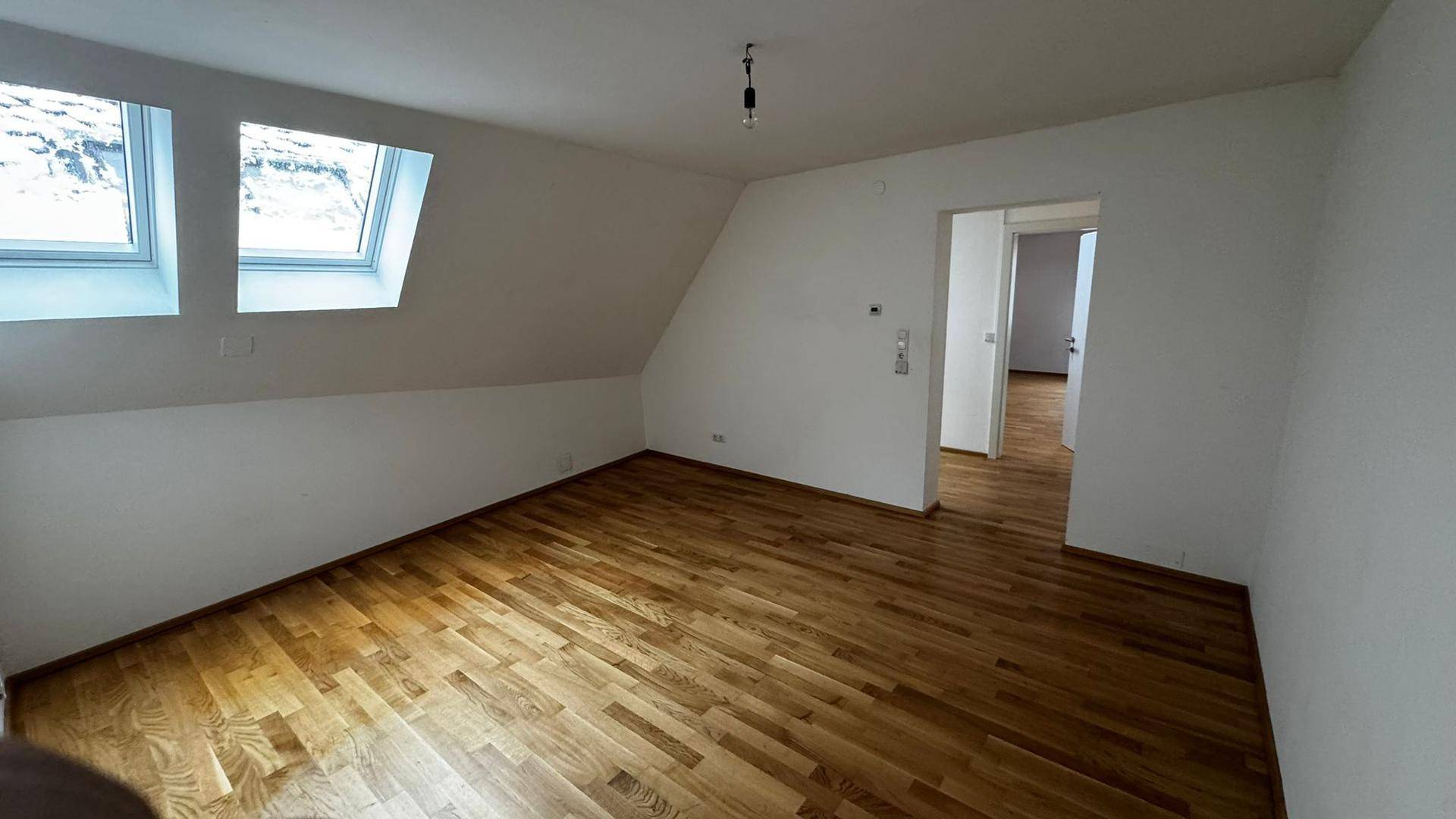 Heller Dachgeschossraum mit Parkettboden, weißen Wänden und zwei Dachfenstern, ideal als Schlafzimmer.