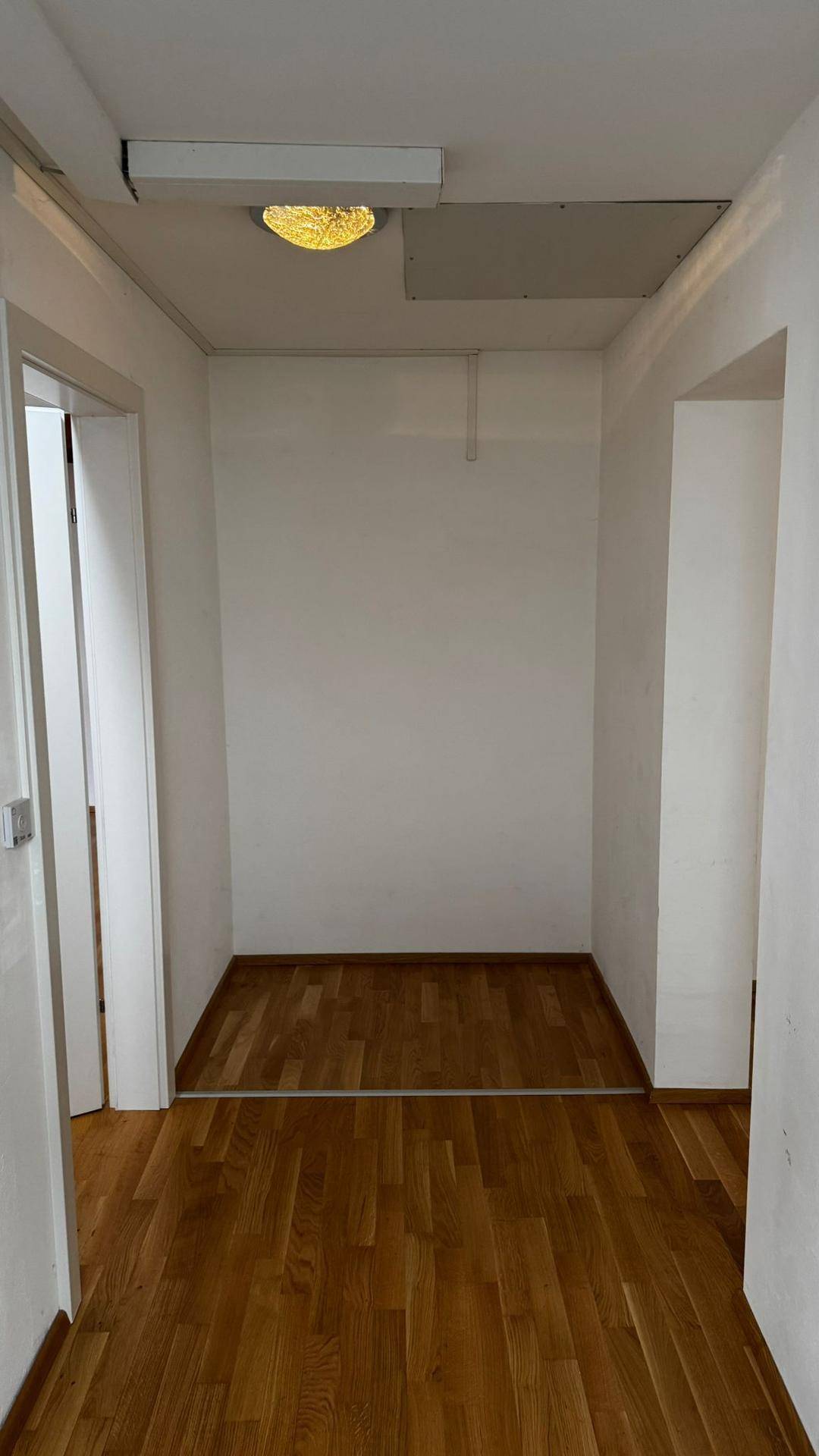 Heller Flur mit Parkettboden und weißen Wänden, der zu weiteren Räumen führt.