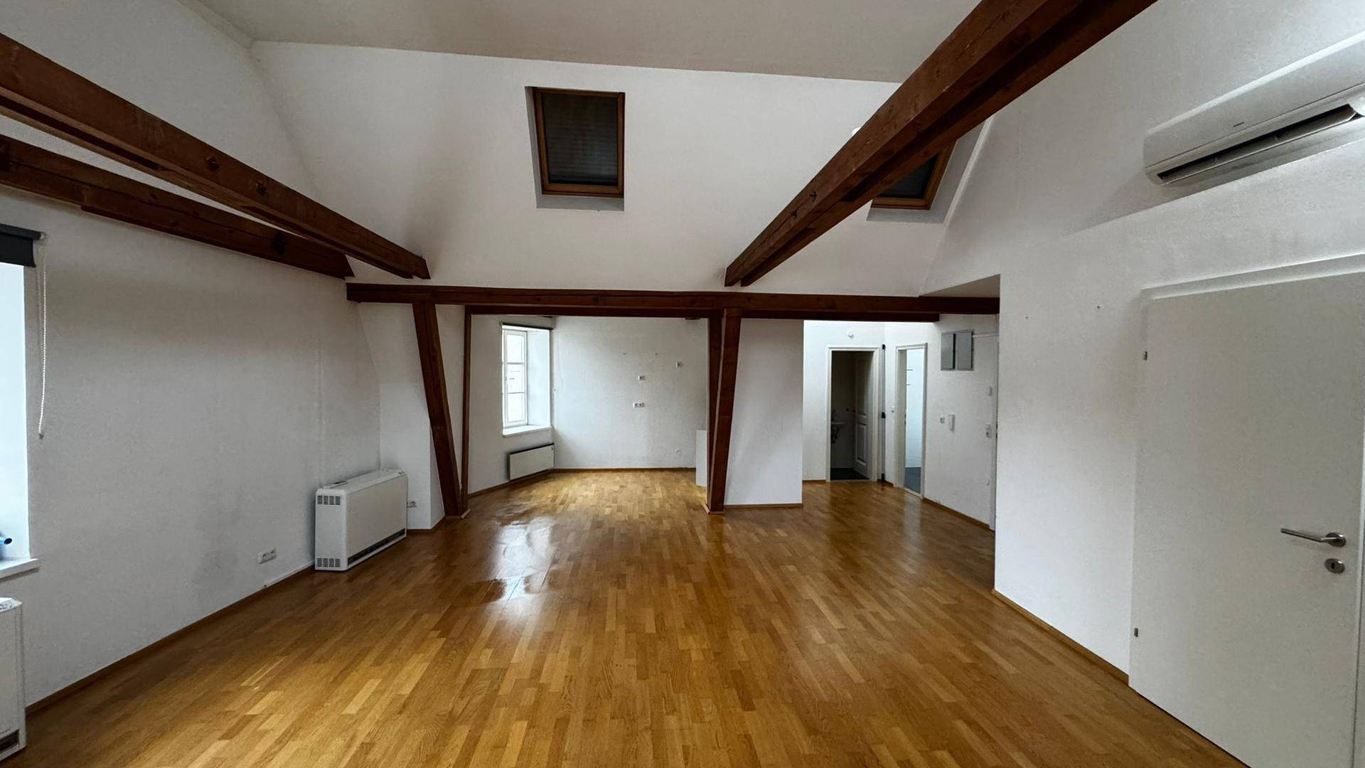 Großer, heller Dachgeschossraum mit Parkettboden, Holzbalken, Dachfenstern und Klimaanlage.