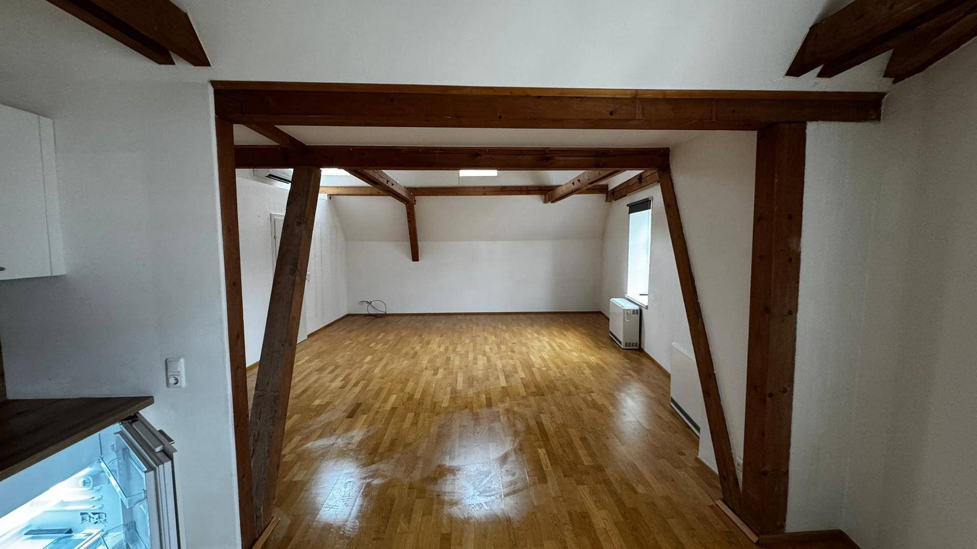 Blick von der Küche in den offenen Wohnbereich mit Parkettboden und sichtbaren Holzbalken im Dachgeschoss.