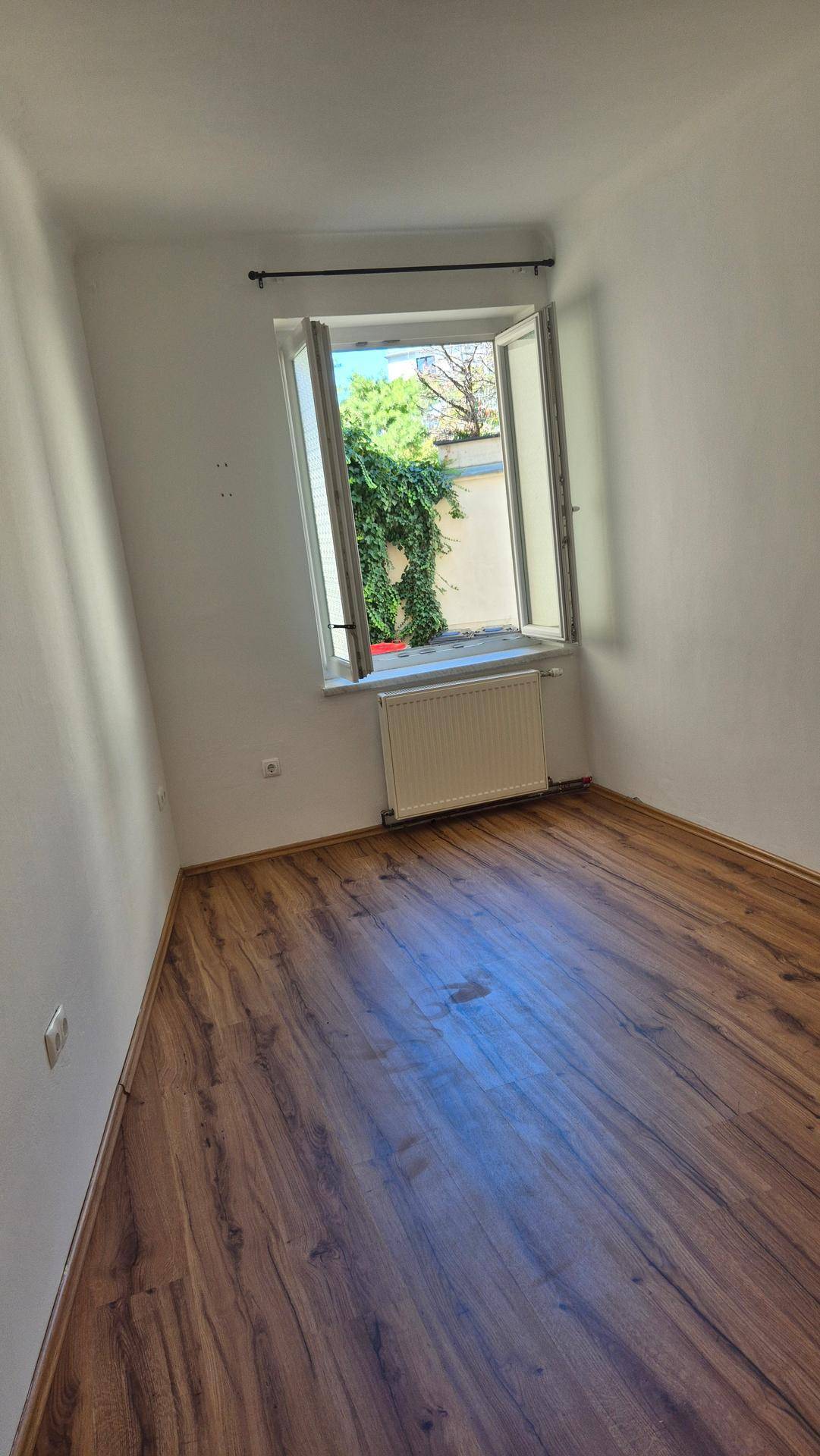 Ruhiges Schlafzimmer mit Laminatboden, weiß gestrichenen Wänden und Blick ins Grüne.