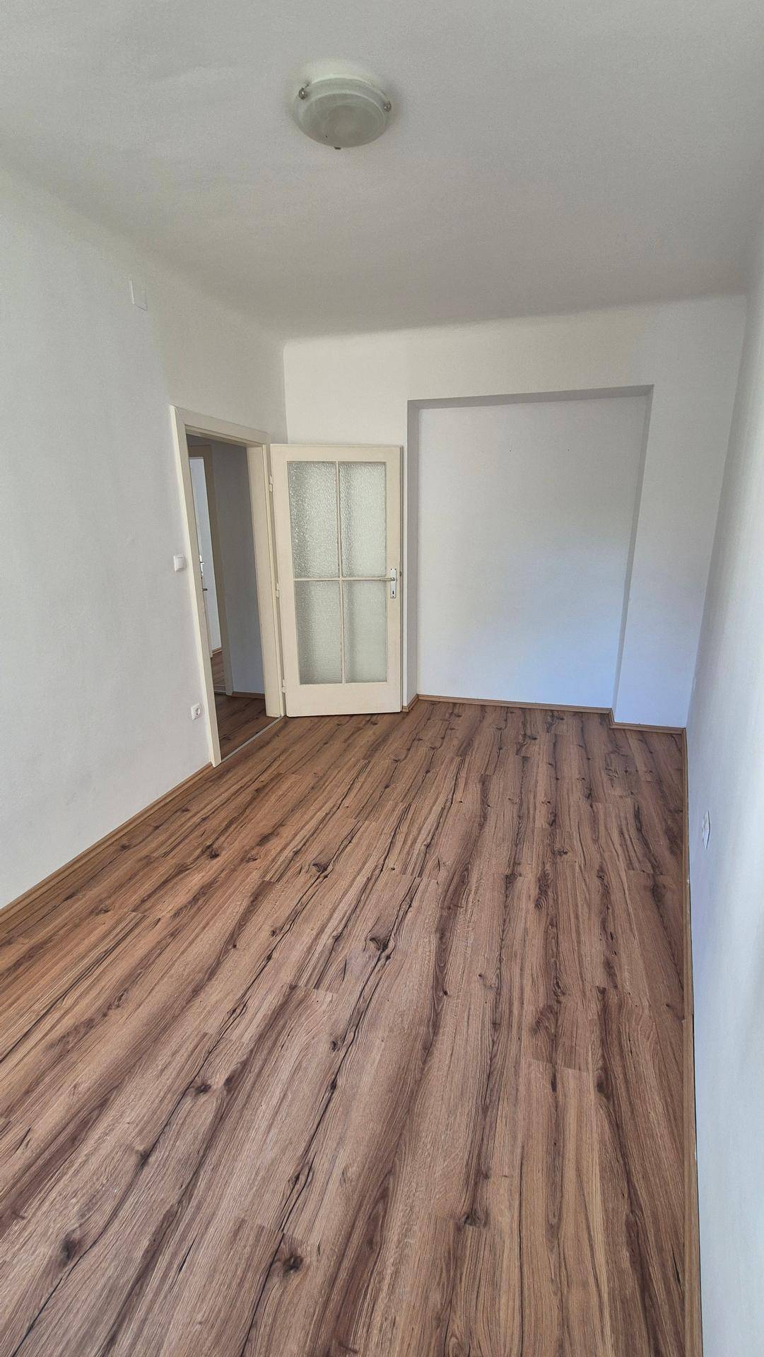 Gemütliches Zimmer mit Laminatboden, weißen Wänden und einer Tür mit Glaseinsätzen.