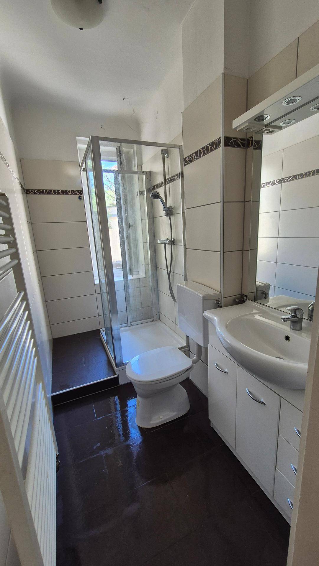 Funktionales Badezimmer mit Duschkabine, WC, Waschbecken und beheiztem Handtuchhalter.