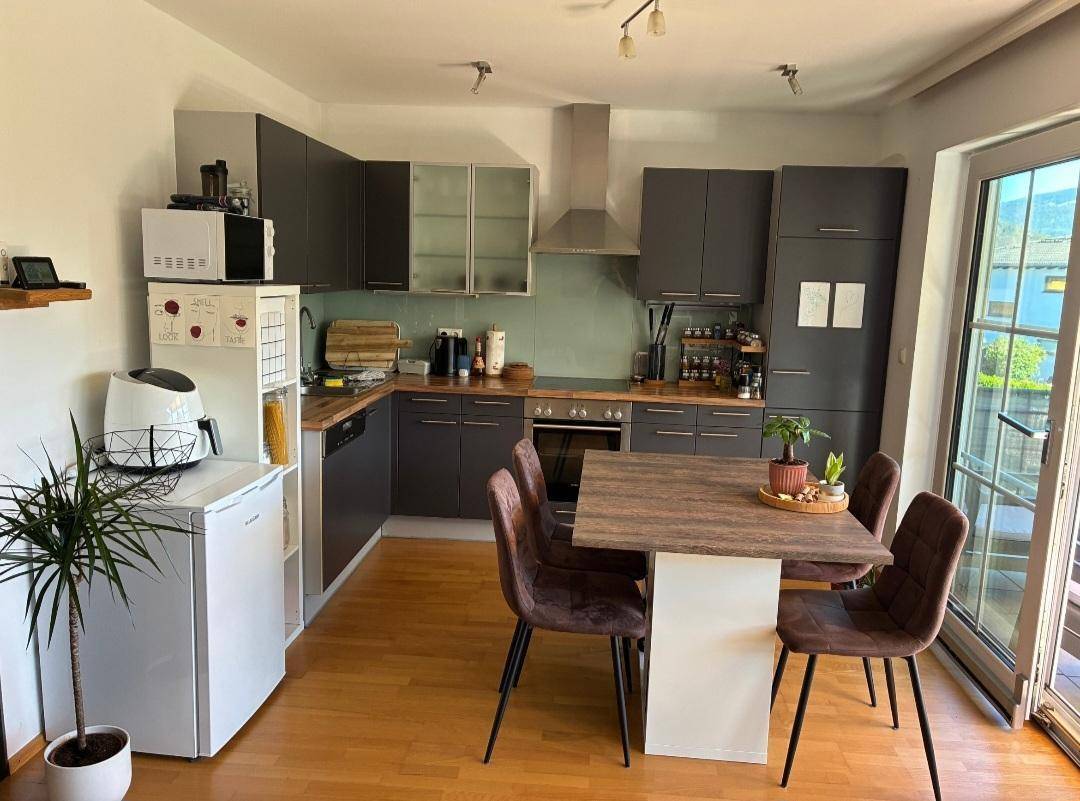 Moderne Küche mit dunkelgrauen Schränken, Holzarbeitsplatte und Essbereich mit Zugang zum Balkon.