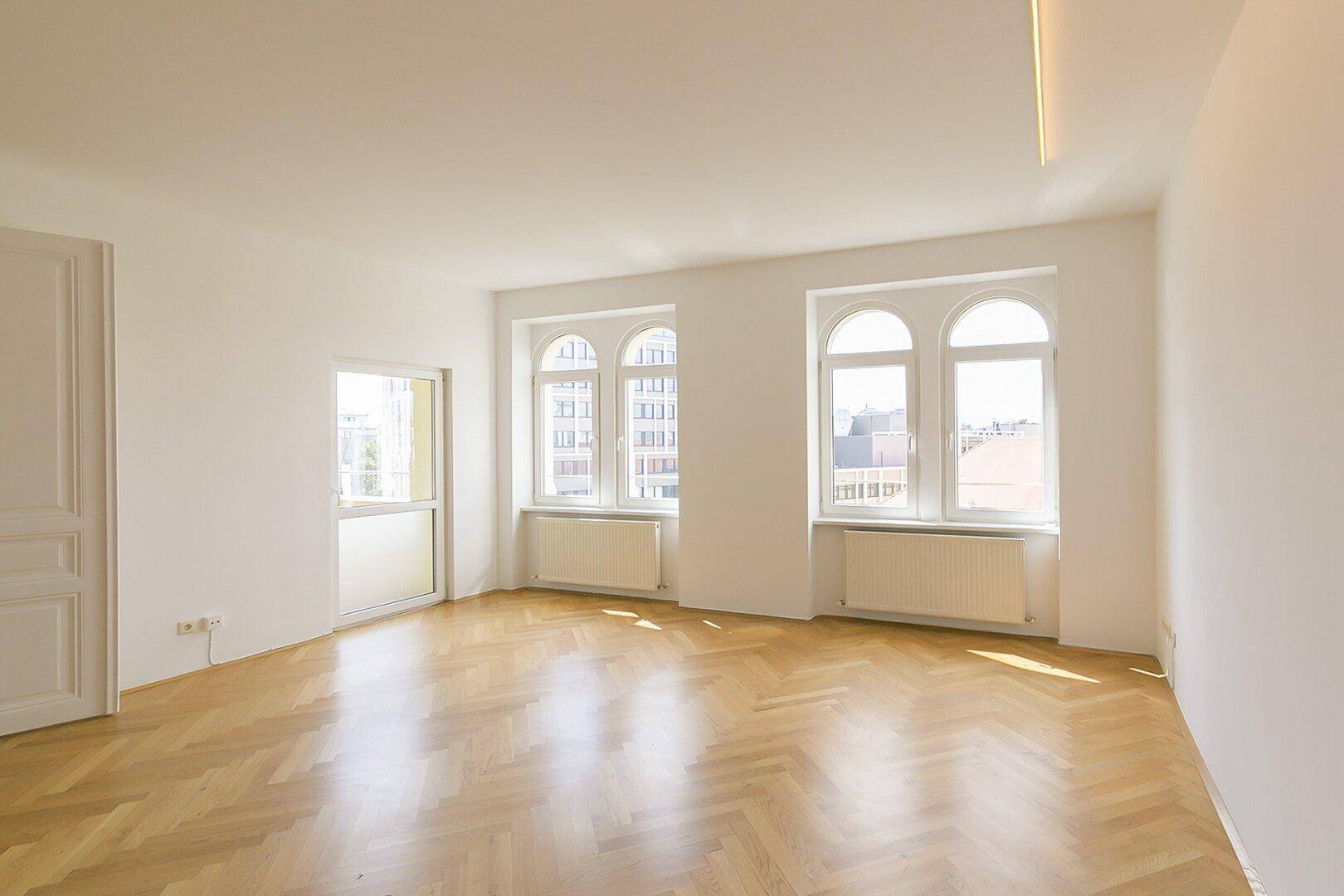 Helles, leeres Zimmer mit Fischgrätparkett und hohen Rundbogenfenstern, bereit zur Gestaltung.