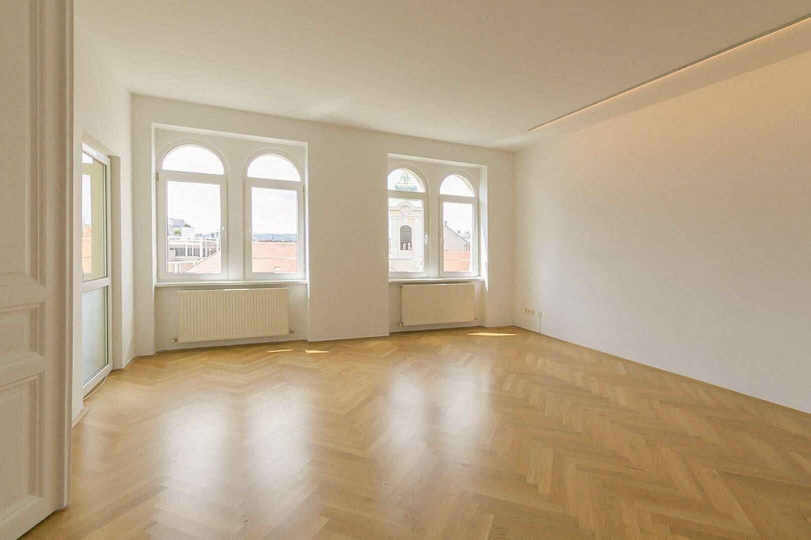 Geräumiges, helles Zimmer mit klassischem Fischgrätparkett und großen Fenstern mit Stadtblick.