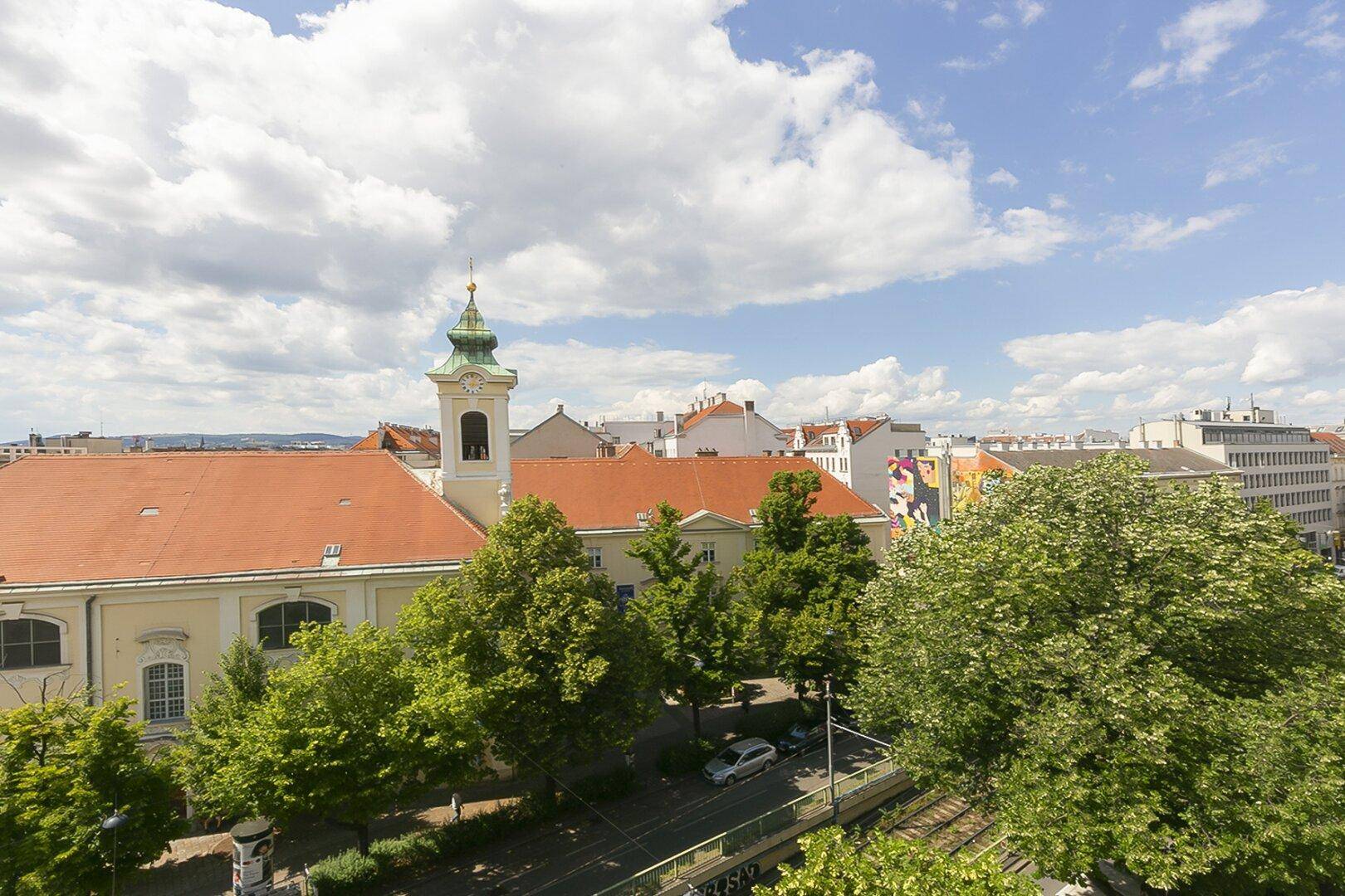 Weitläufiger Blick über die Dächer der Stadt mit einer historischen Kirche und viel Grün.