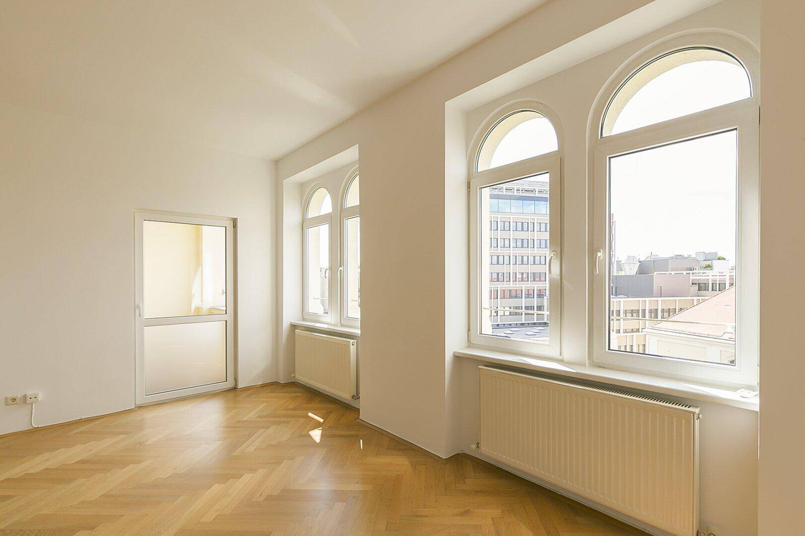 Lichtdurchflutetes Zimmer mit elegantem Fischgrätparkett und Zugang zu einem Außenbereich.