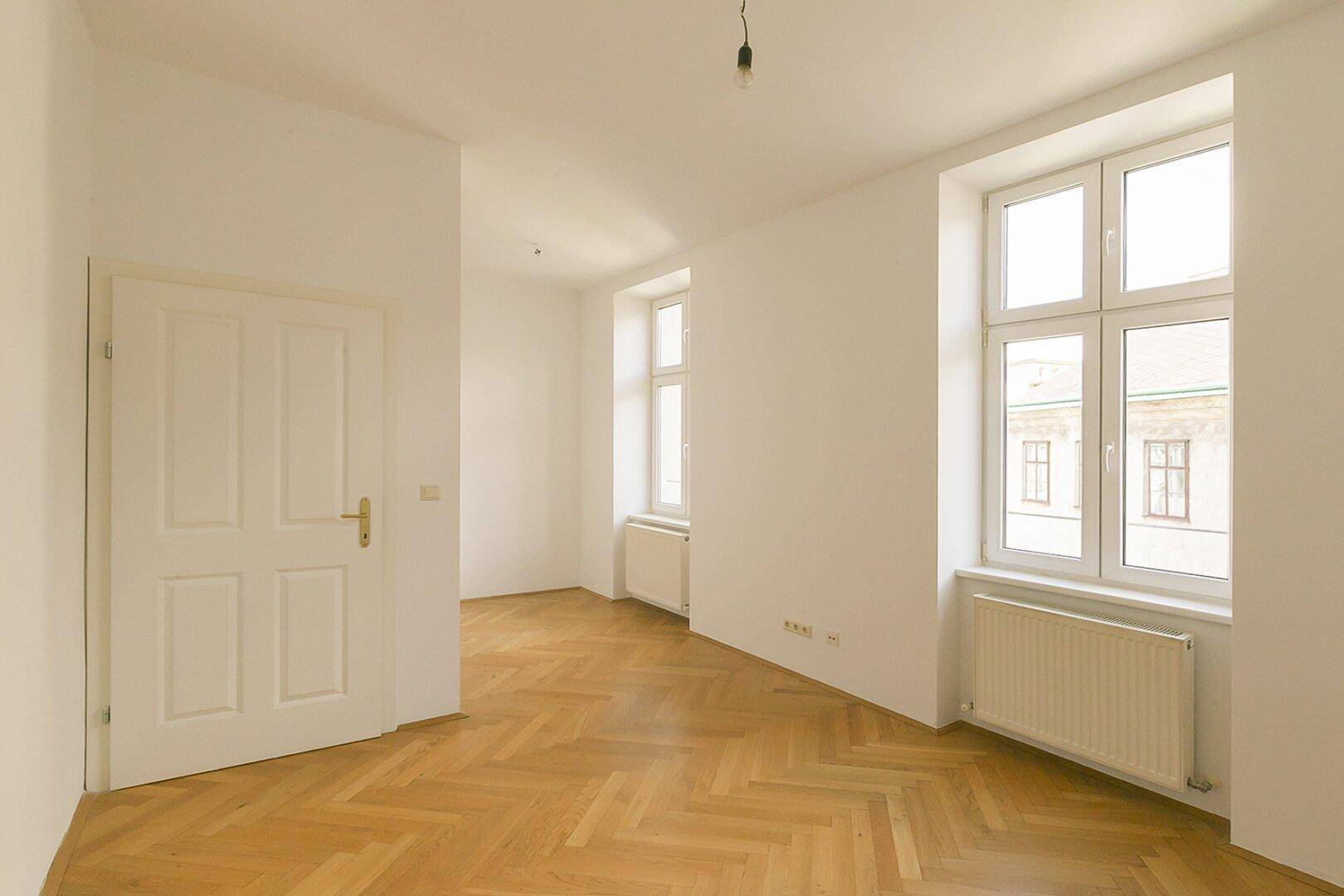 Helles Schlafzimmer mit Fischgrätparkett und großen Fenstern, ideal für ruhige Stunden.