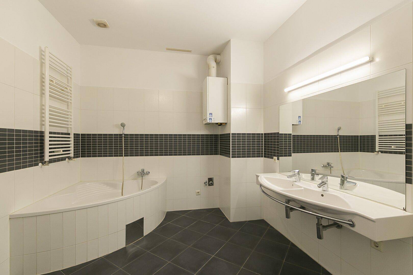 Geräumiges Badezimmer mit Badewanne, Doppelwaschbecken und dunklen Fliesenakzenten.