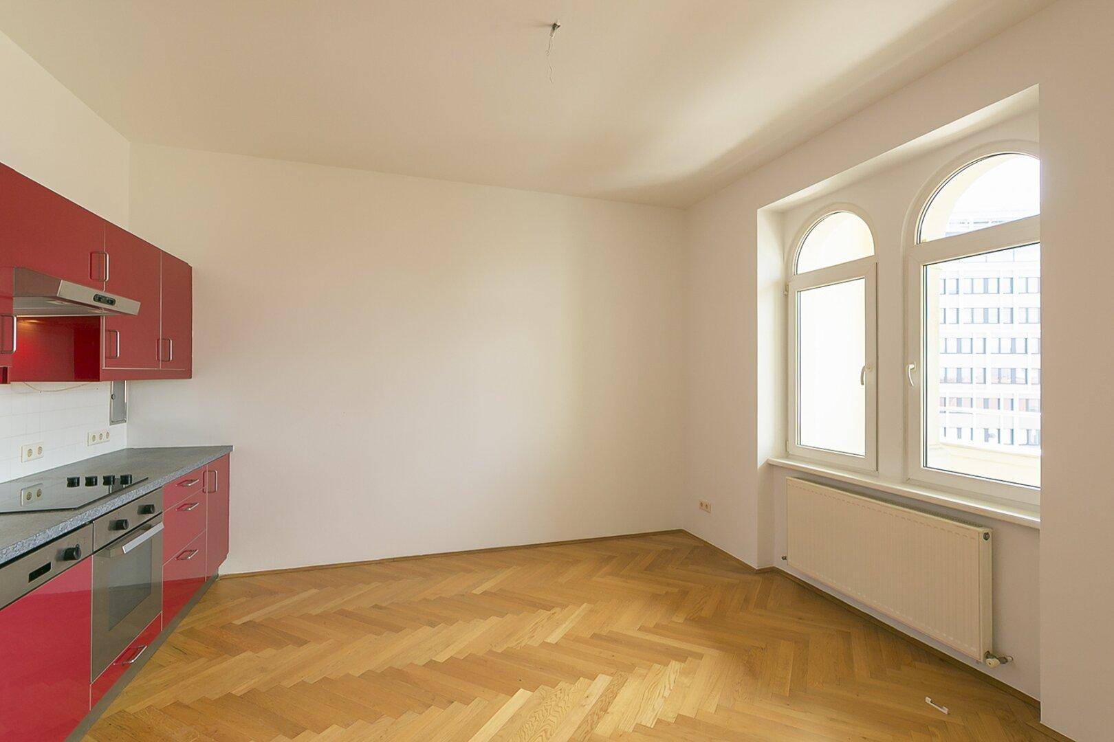 Offene Küche mit roten Schränken und angrenzendem Essbereich mit Fischgrätparkett.