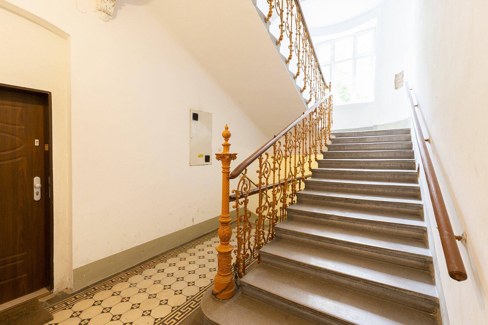 Historisches Treppenhaus mit kunstvollem Geländer und gemusterten Fliesen im Eingangsbereich.
