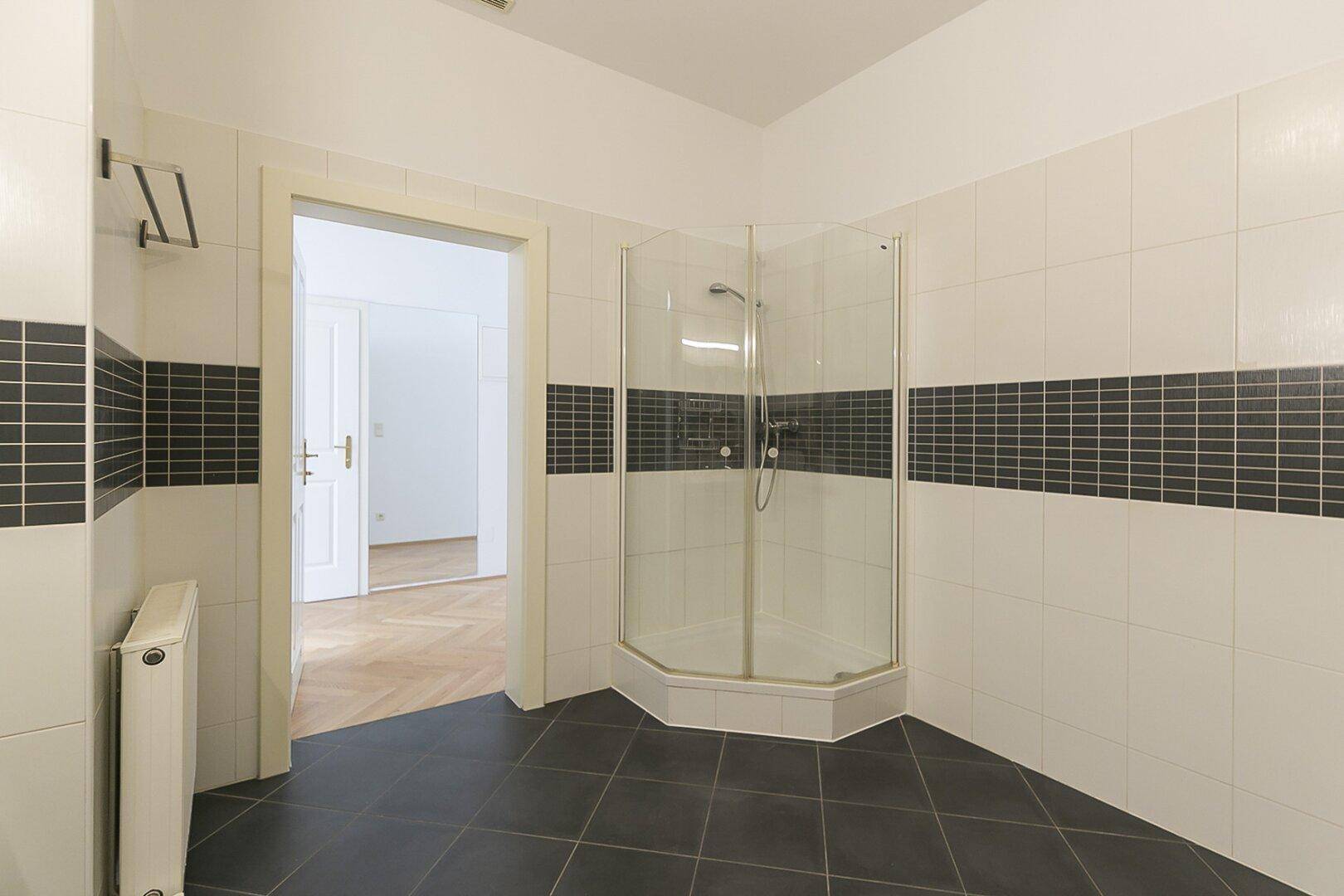 Modernes Badezimmer mit Duschkabine, dunklen Fliesen und Zugang zu einem weiteren Raum.