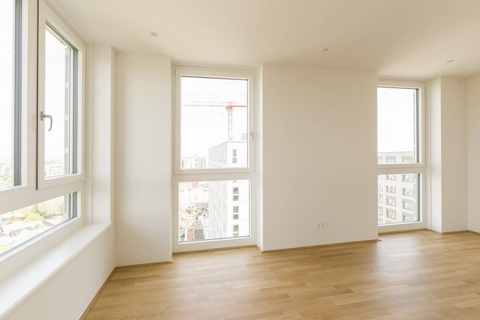 Geräumiger Wohnbereich mit hellen Wänden und großen Fenstern, die einen Blick auf die umliegenden Gebäude ermöglichen.