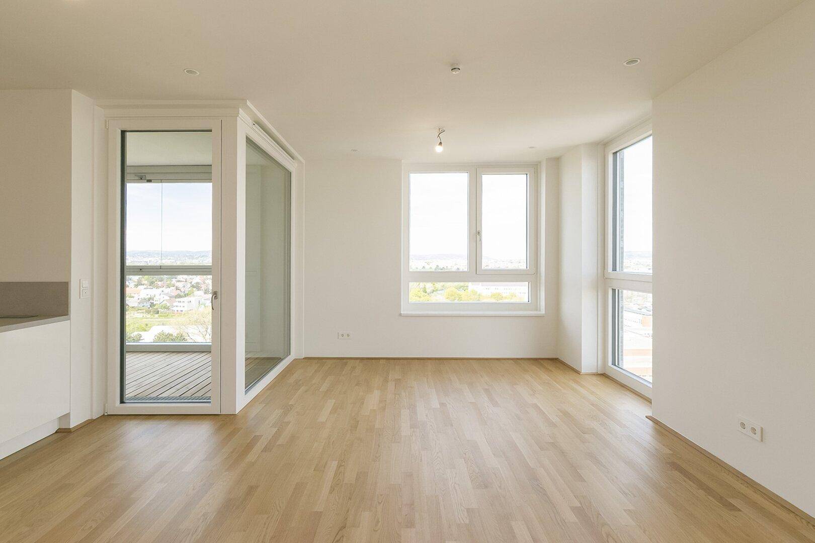 Heller Wohnbereich mit Parkettboden und großen Fenstern, die viel Tageslicht hereinlassen und eine weite Aussicht bieten.