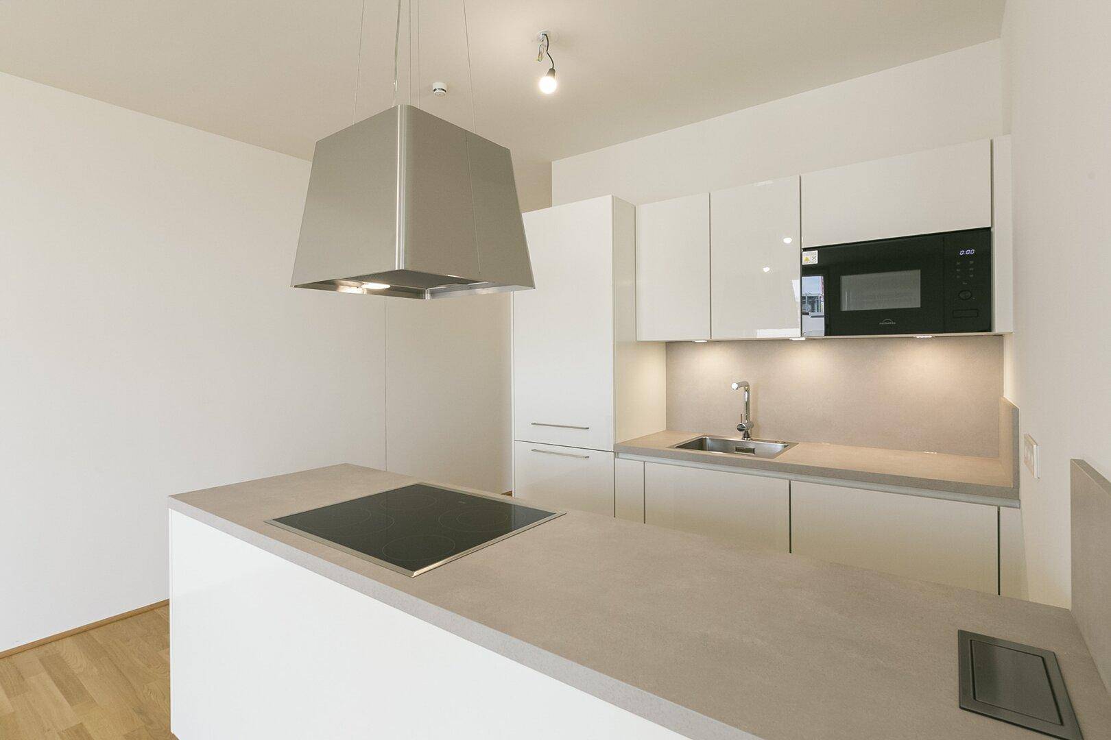 Moderne Einbauküche mit weißen Hochglanzfronten, Kochinsel und integrierten Geräten in hellem Raum.