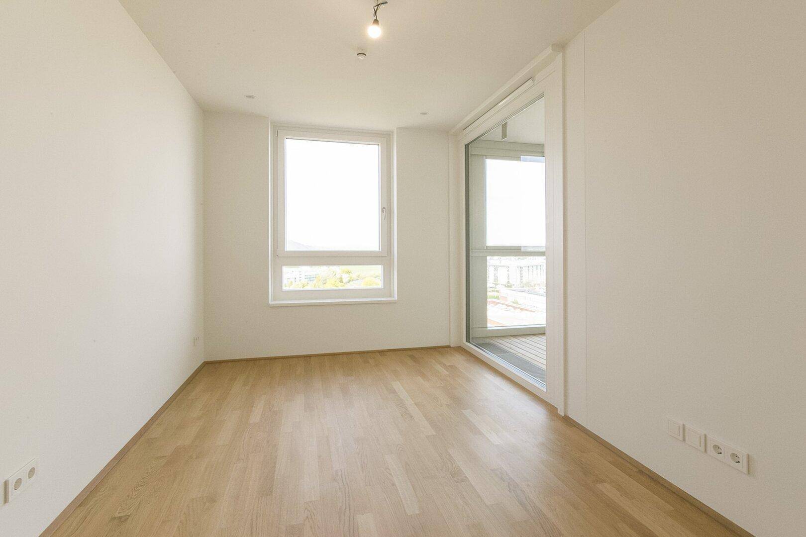 Geräumiges Schlafzimmer mit Parkettboden und Zugang zu einer verglasten Loggia, die zusätzlichen Raum bietet.