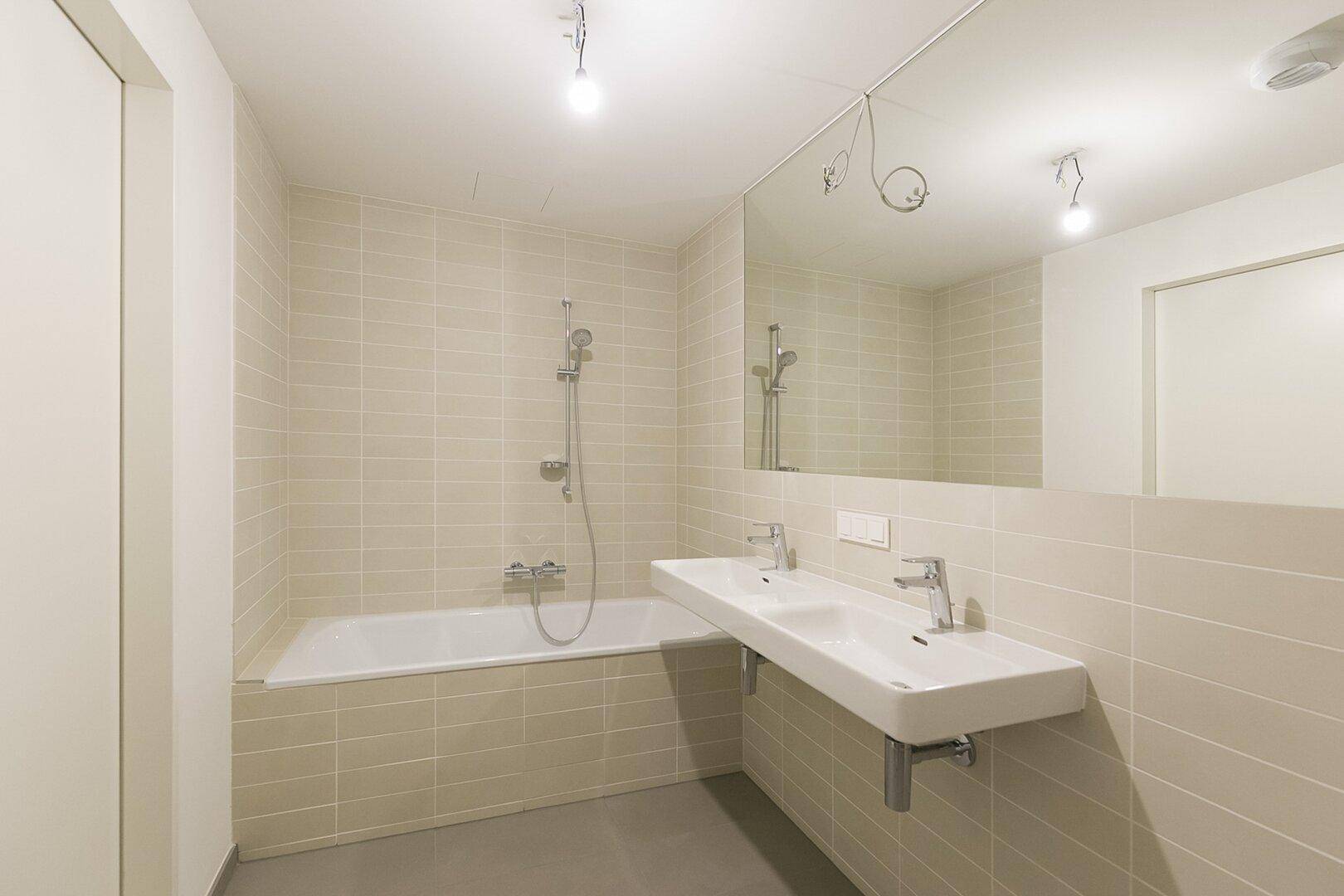 Modernes Badezimmer mit Doppelwaschbecken, Badewanne und hellen Fliesen an den Wänden.