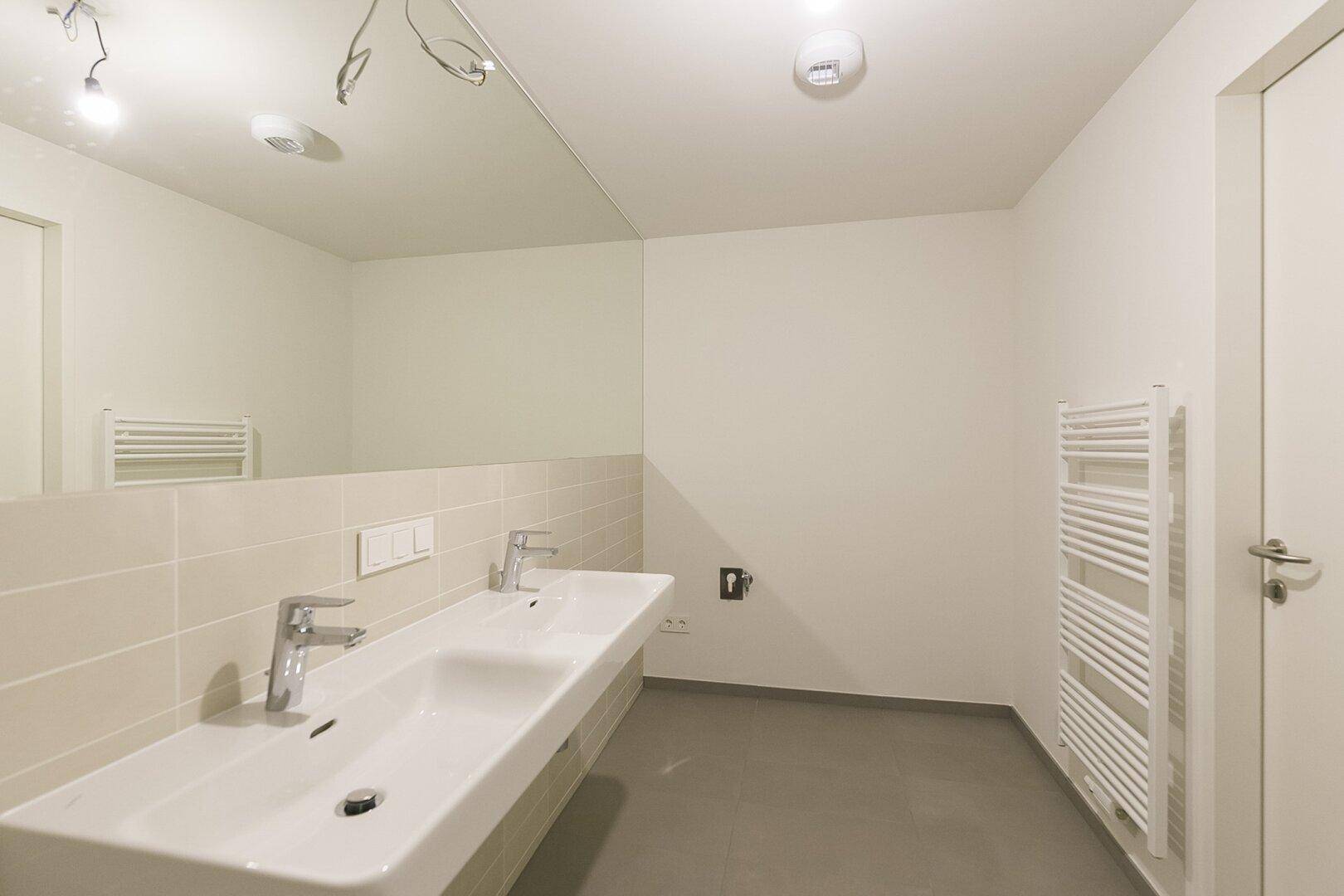 Modernes Badezimmer mit Doppelwaschbecken, beheiztem Handtuchhalter und großen Spiegeln.