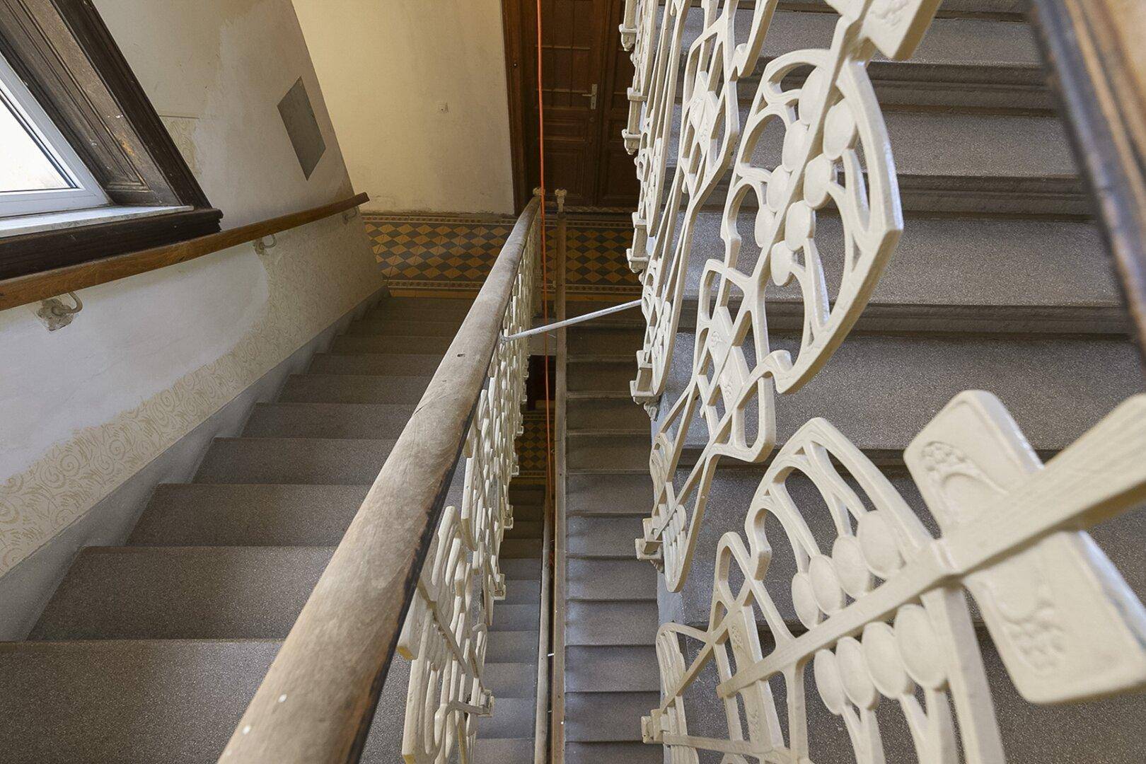 Historisches Treppenhaus mit kunstvollen Geländern und gemusterten Fliesen auf den Podesten.