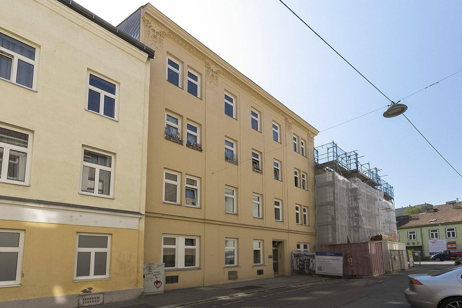Straßenansicht eines historischen Gebäudes mit heller Fassade und angrenzender Baustelle.