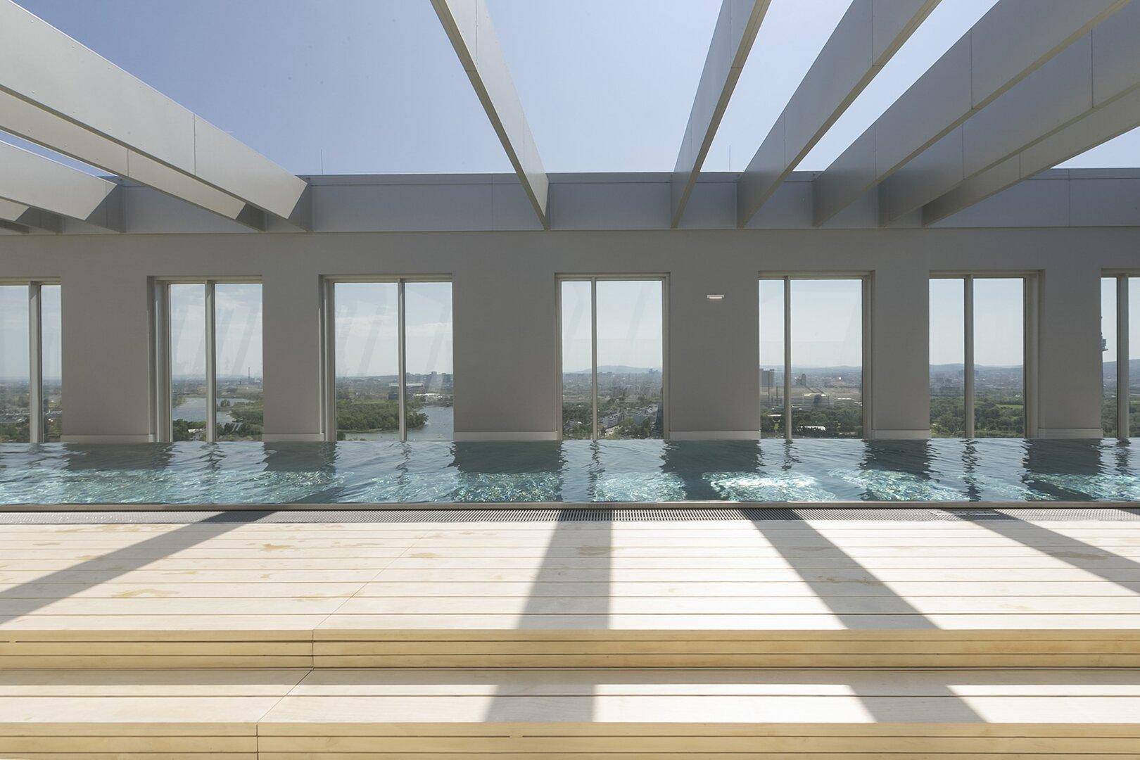 Exklusiver Dachpool mit Holzdeck und Panoramablick über die Stadt unter blauem Himmel.
