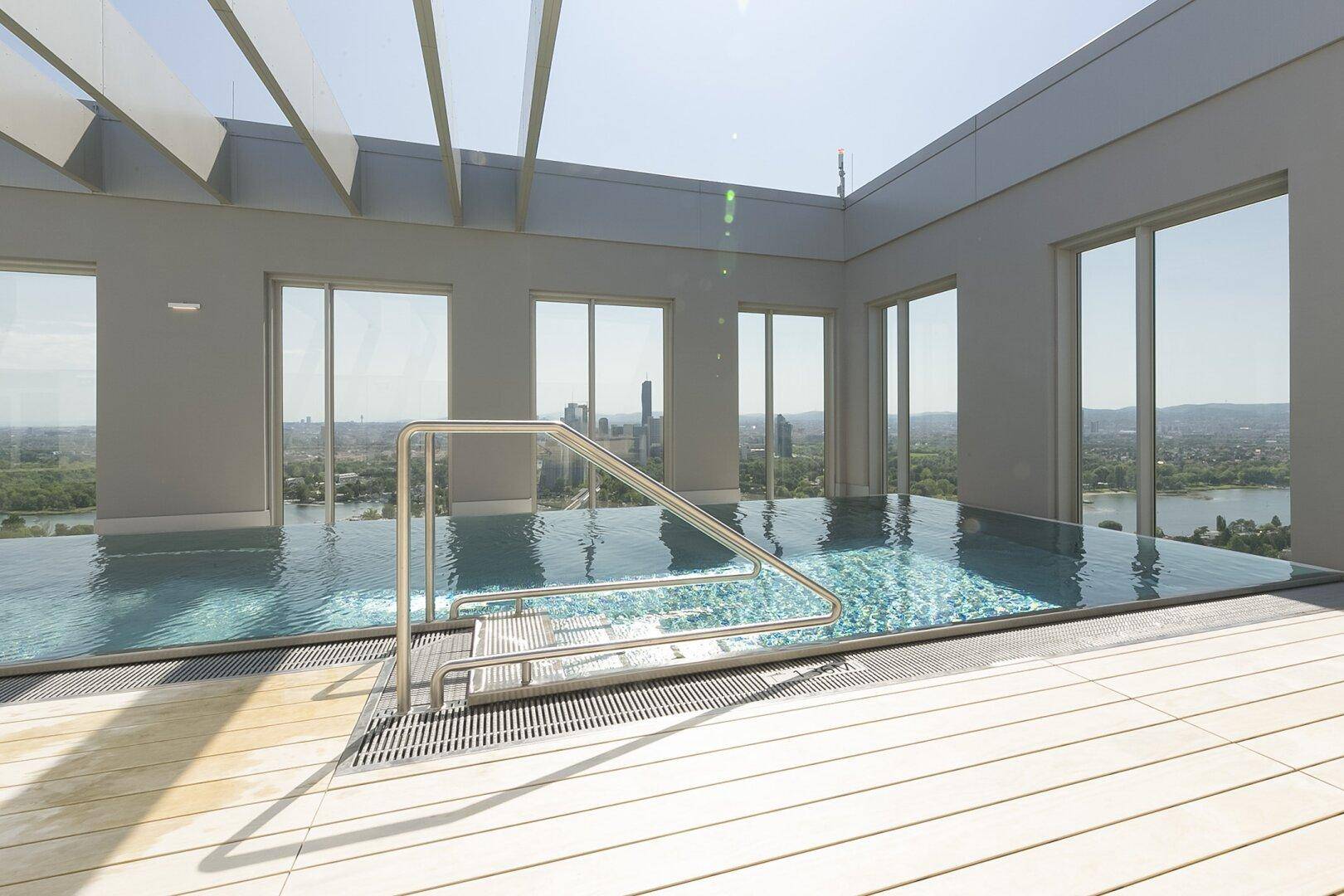 Moderner Dachpool mit glitzerndem Wasser und beeindruckendem Stadtblick, umgeben von einer Holzterrasse.
