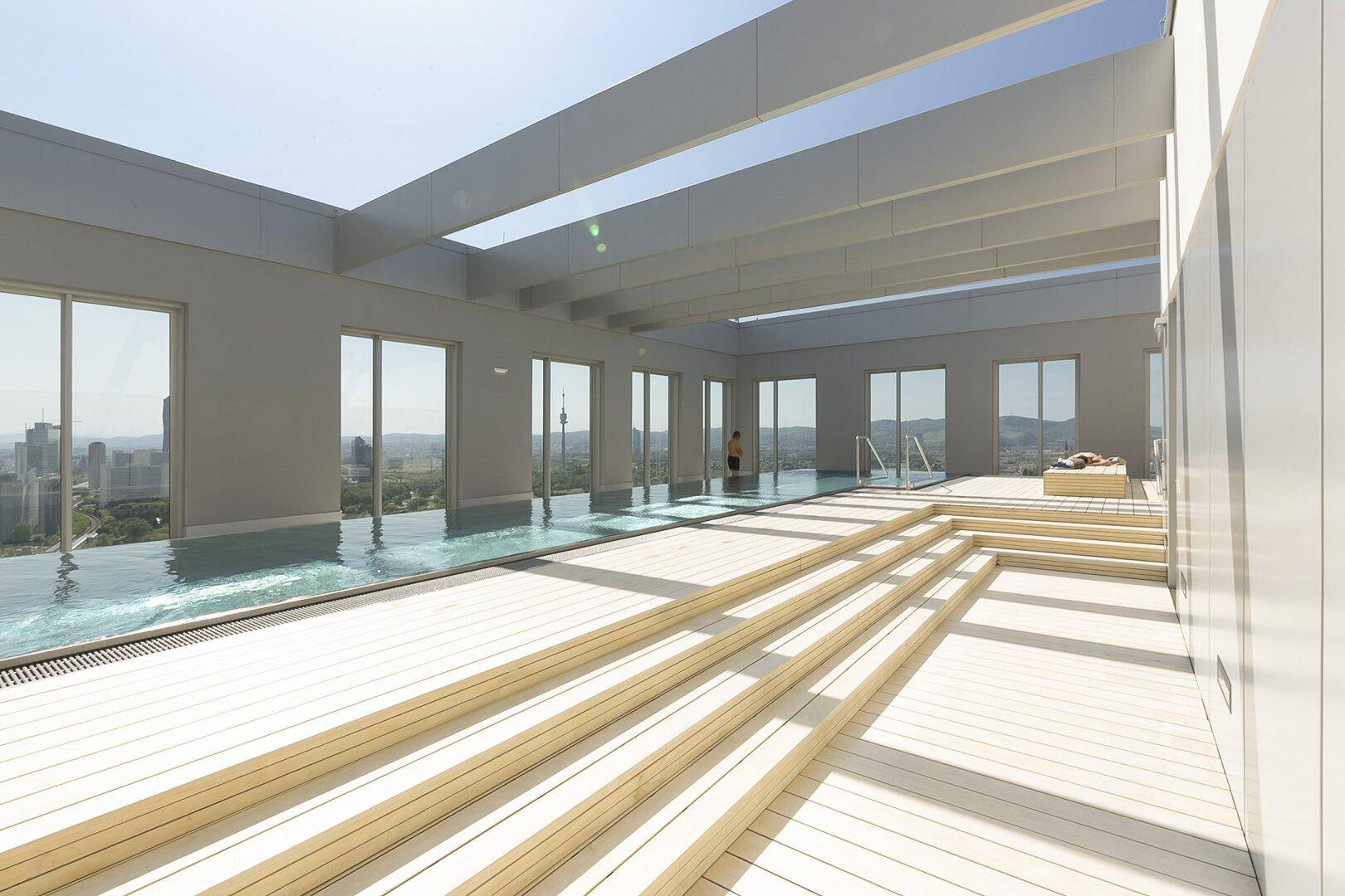 Luxuriöser Dachpoolbereich mit Holzdeck, Liegeflächen und weitem Blick über die Stadtlandschaft.