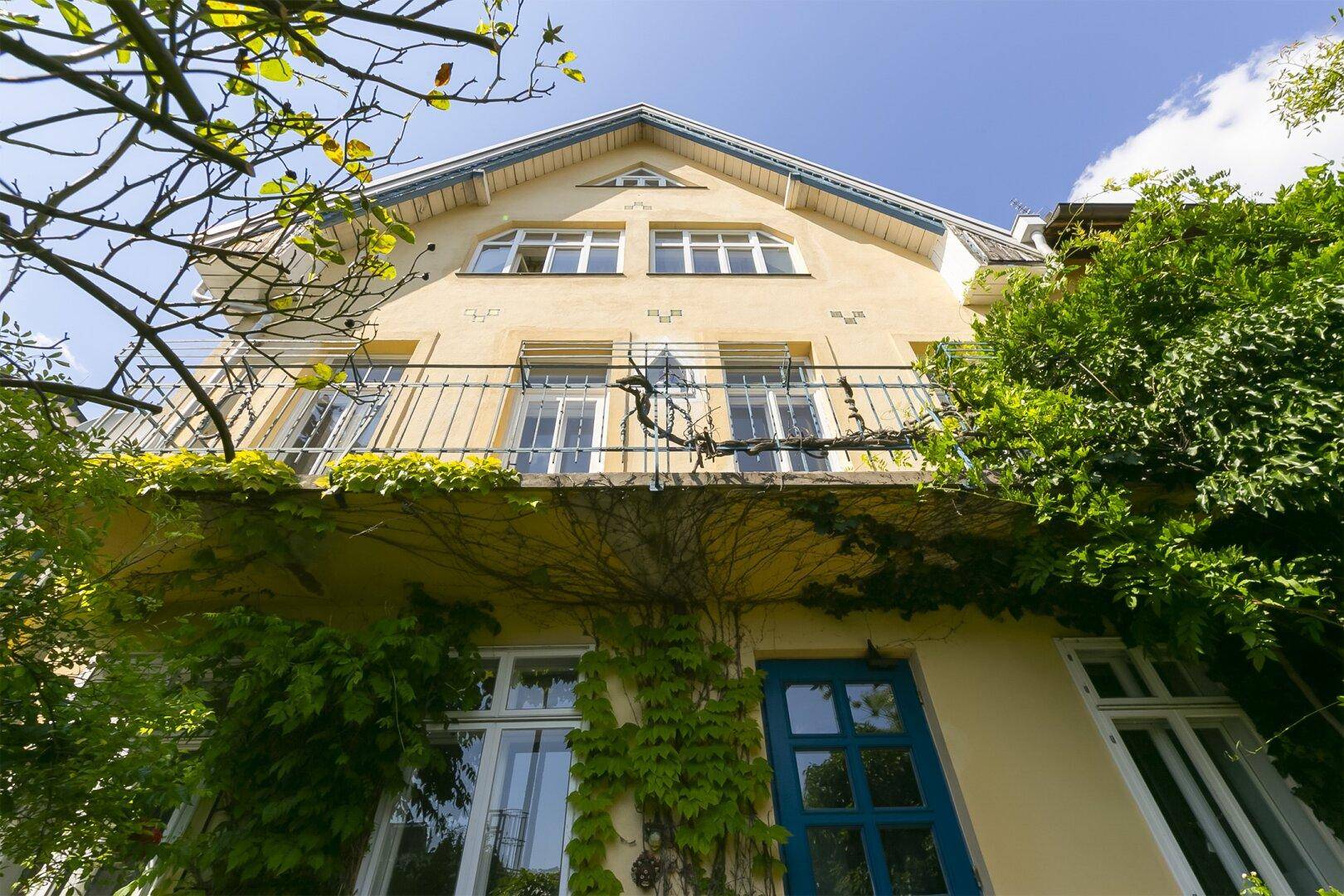Gelbe Hausfassade mit Balkon, vielen Fenstern und üppigem Efeubewuchs.
