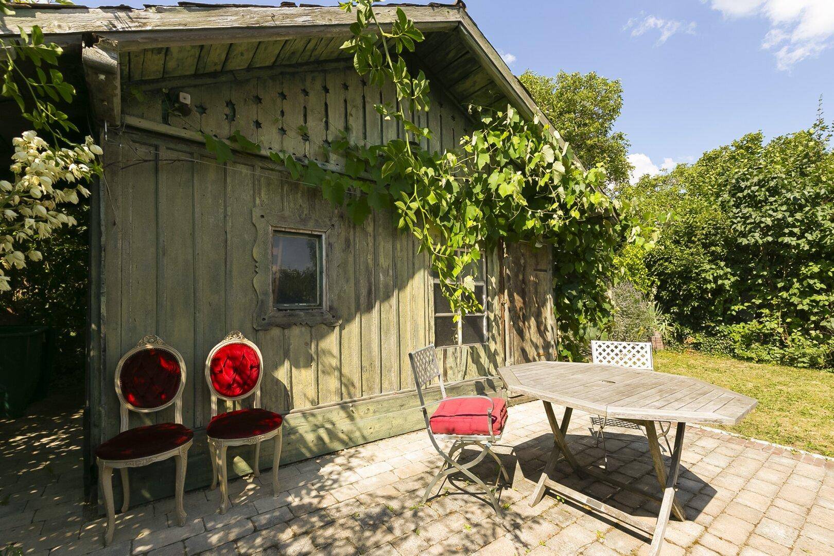 Gemütlicher Sitzbereich im Garten mit rustikalen Möbeln vor einem Holzschuppen.