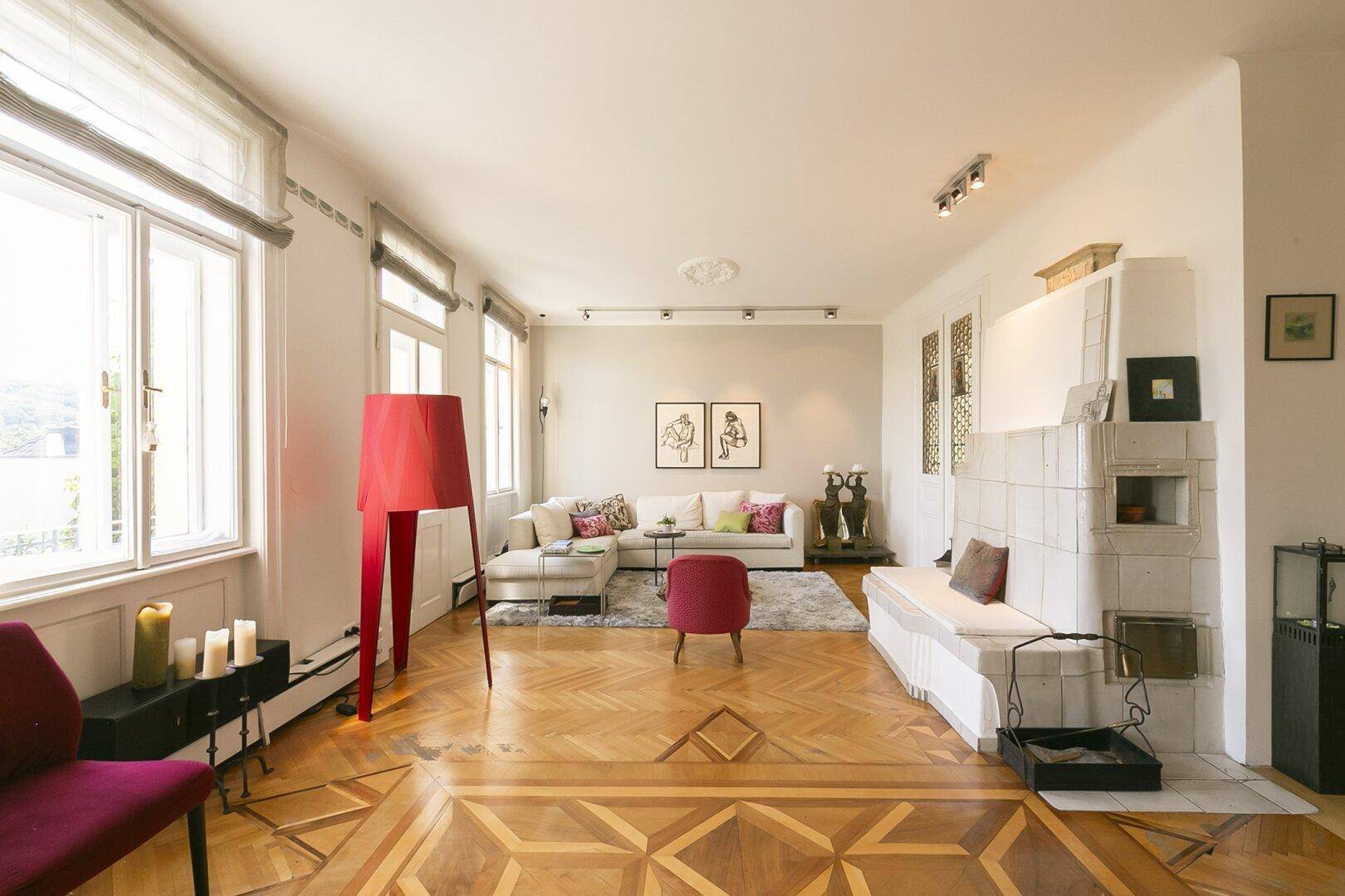 Elegantes Wohnzimmer mit gemustertem Parkett, Kachelofen und großen Fenstern für viel Licht.
