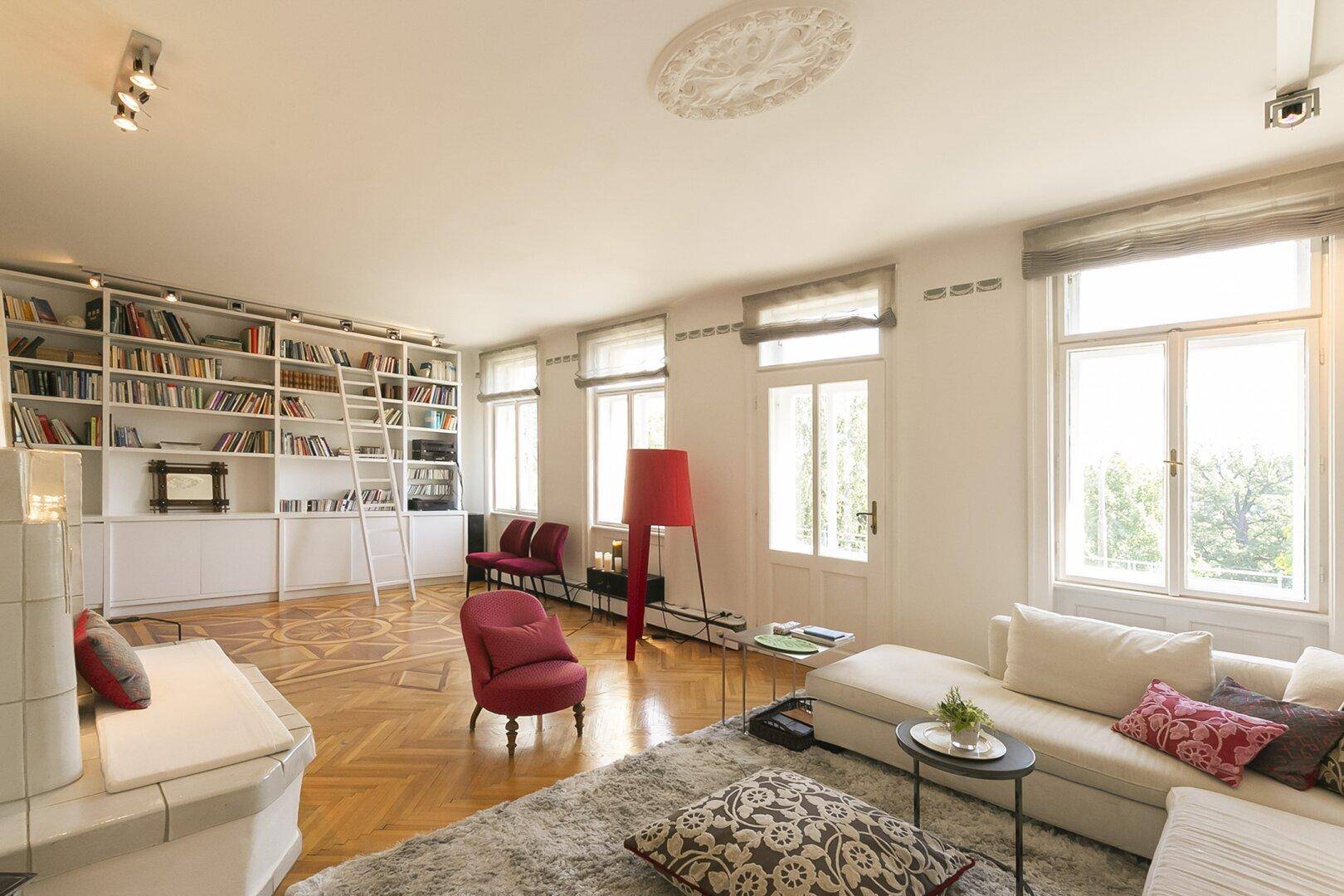 Helles Wohnzimmer mit Fischgrätparkett, großem Bücherregal und gemütlicher Sitzecke.