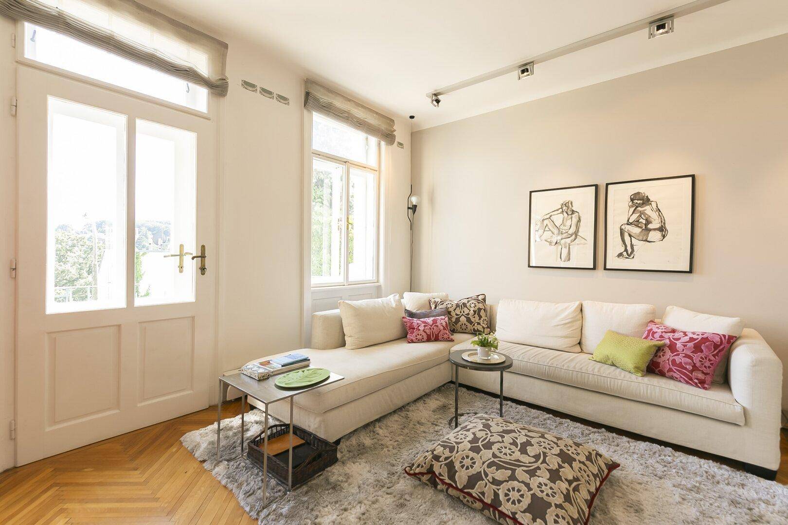 Gemütliche Sitzecke im Wohnzimmer mit hellem Sofa, Kissen und Zugang zu einem Balkon.