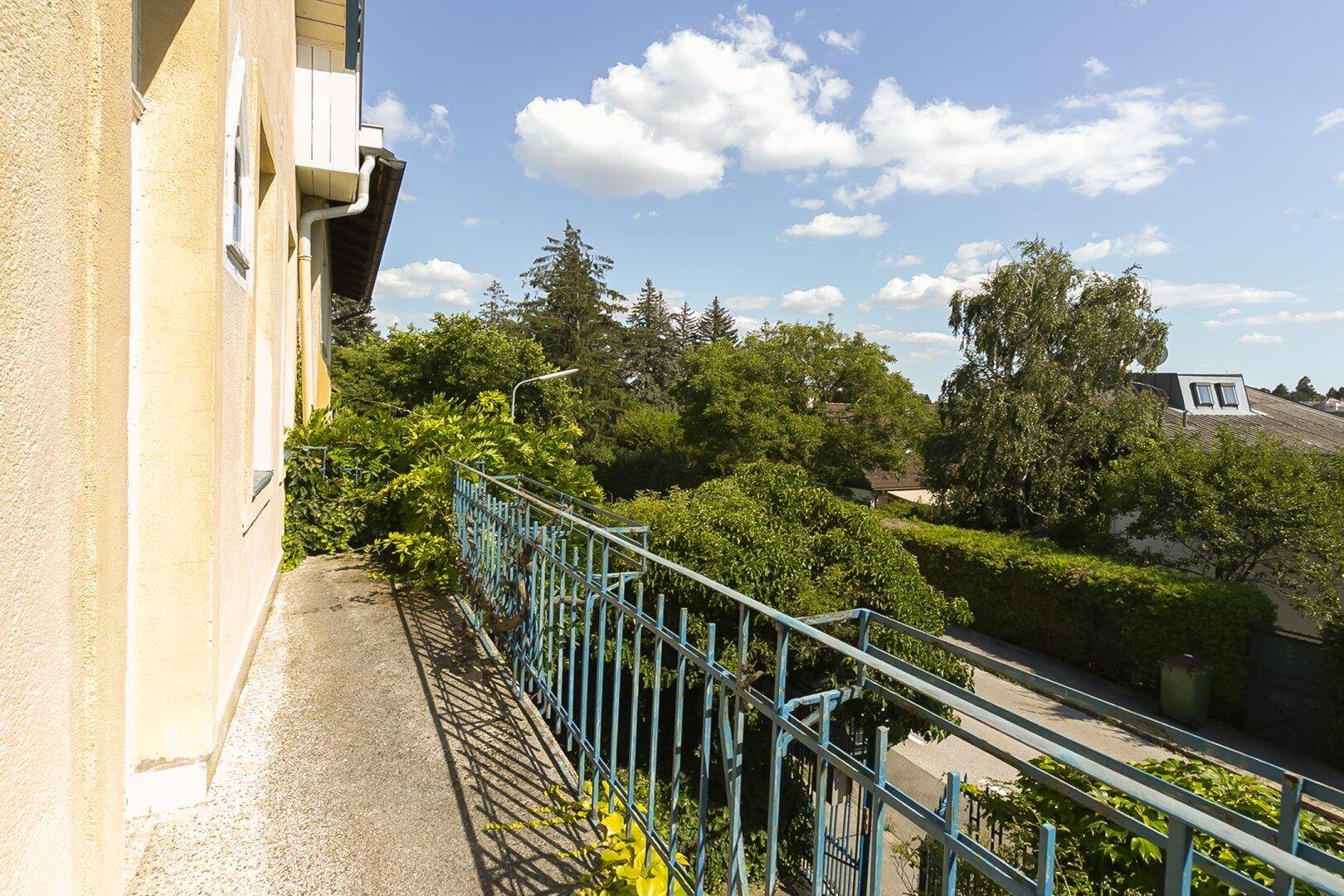 Schmaler Balkon mit blauem Geländer und Blick auf die grüne Umgebung und die Straße.
