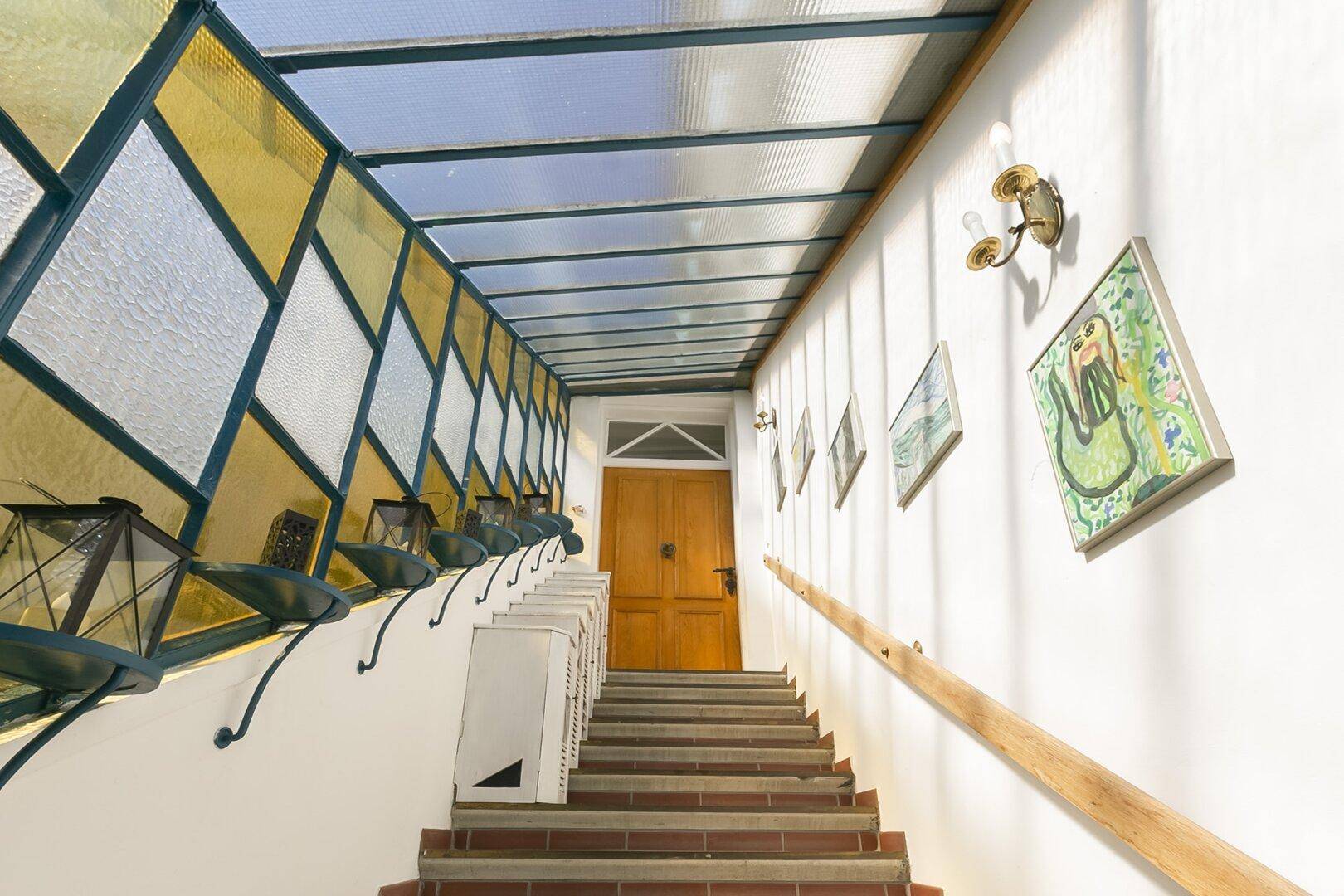 Treppenhaus mit Holzgeländer, hellen Wänden und einem Glasdach für viel Tageslicht.