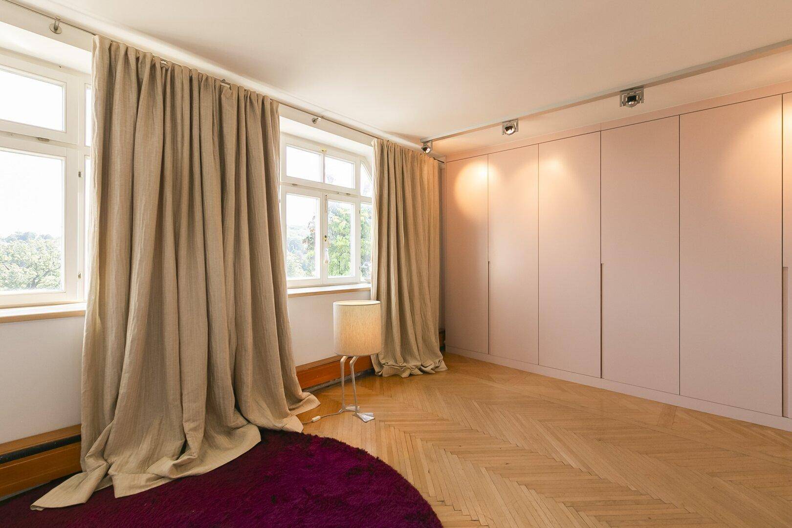 Helles Schlafzimmer mit großen Fenstern, Vorhängen und Einbauschränken.