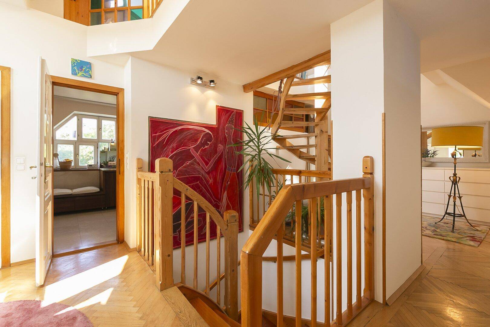 Heller Flur mit Holztreppe, Kunstwerken und Blick in angrenzende Räume.