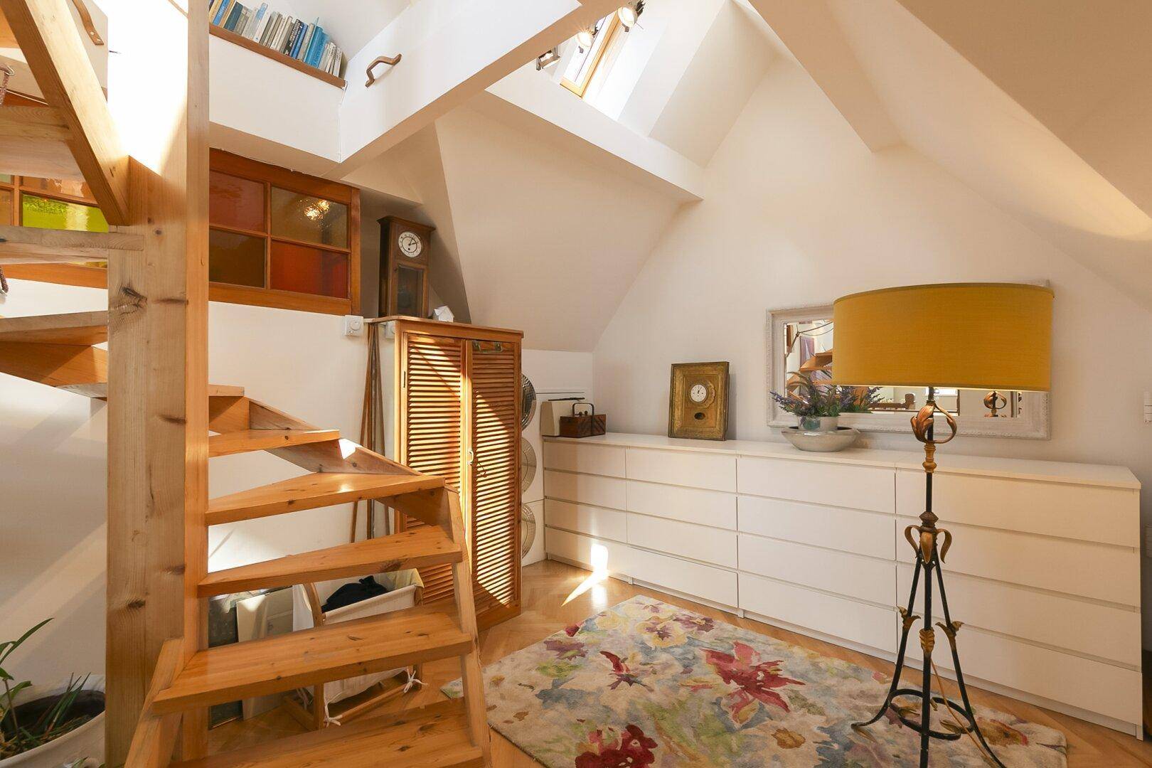 Dachgeschossbereich mit Holztreppe, Dachfenstern und Stauraum.