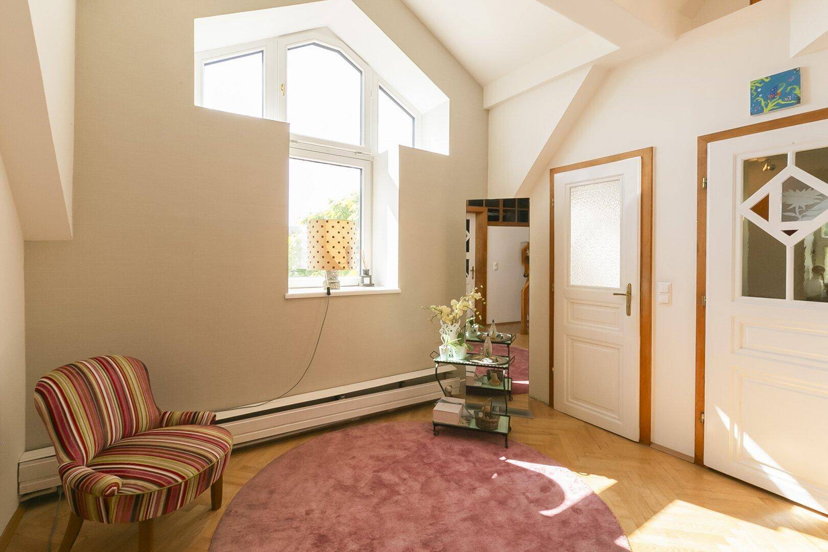 Heller Flur mit großen Fenstern, Sitzgelegenheit und Holzboden.