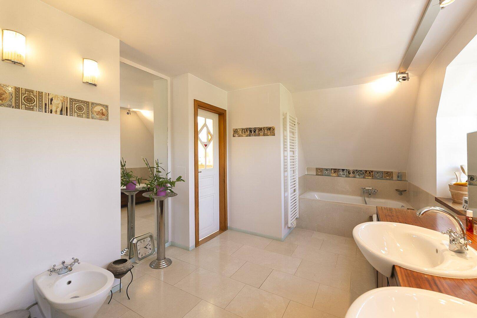 Helles Badezimmer mit Bidet, Badewanne und Doppelwaschbecken auf Holzplatte.