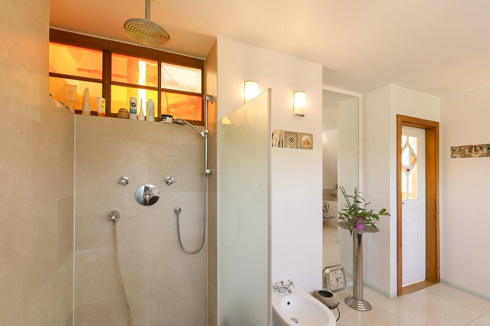 Badezimmer mit moderner Dusche, Bidet und farbigen Glasfenstern.
