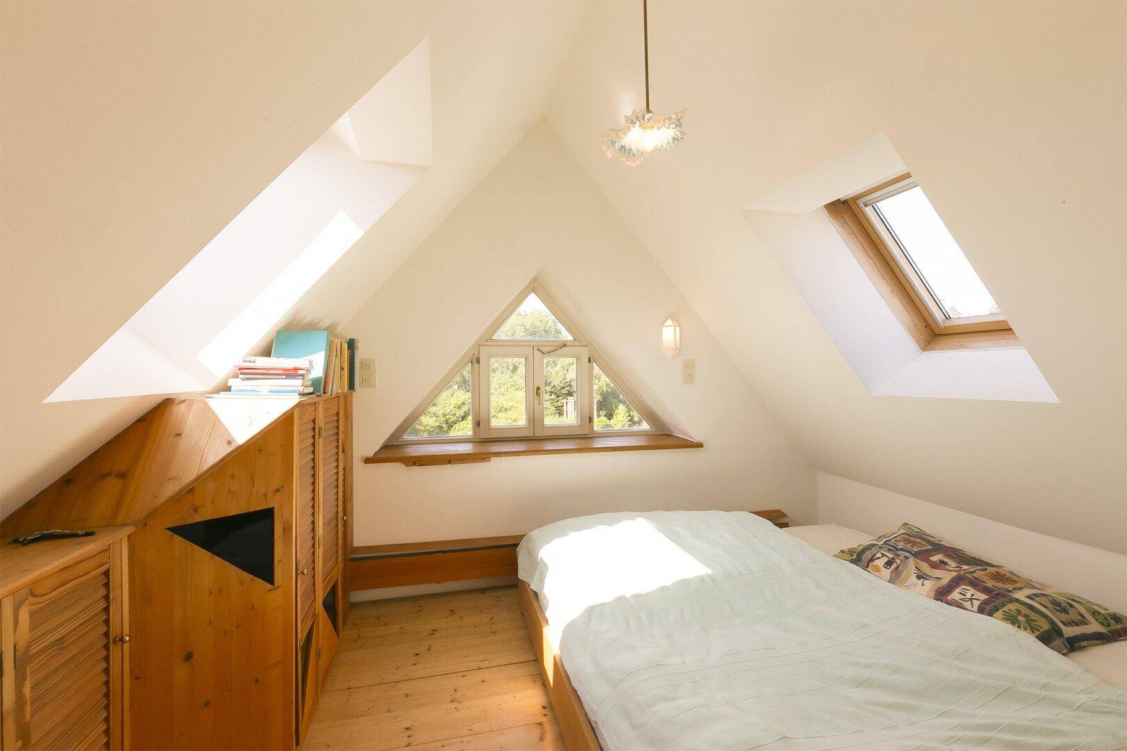 Gemütliches Schlafzimmer im Dachgeschoss mit Holzboden und dreieckigem Fenster.