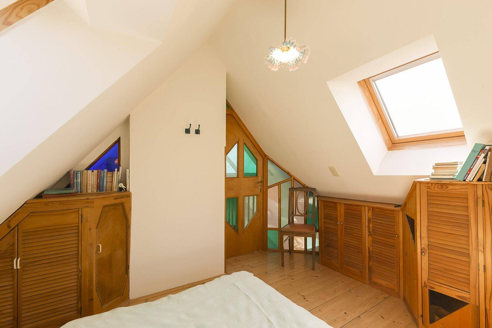 Dachgeschoss-Schlafzimmer mit Holzboden, Dachfenster und integrierten Schränken.