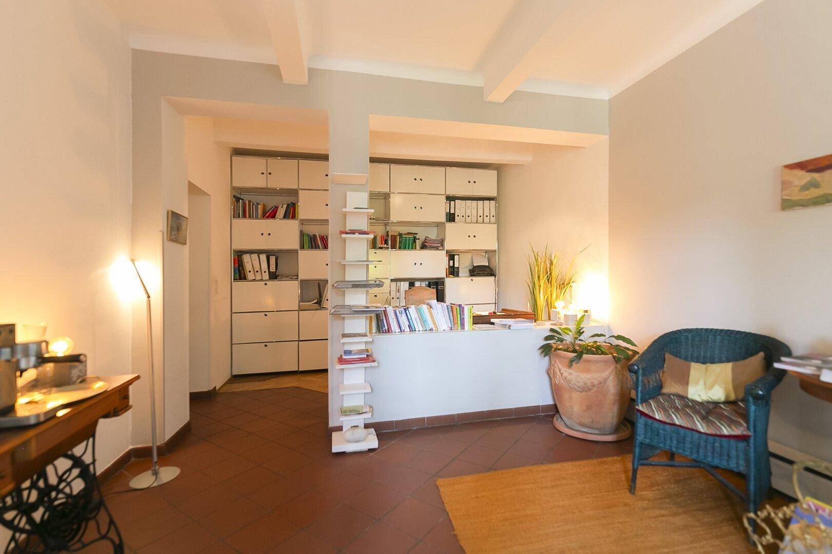 Arbeitszimmer mit Bücherregalen, Terrakottafliesen und gemütlicher Sitzecke.