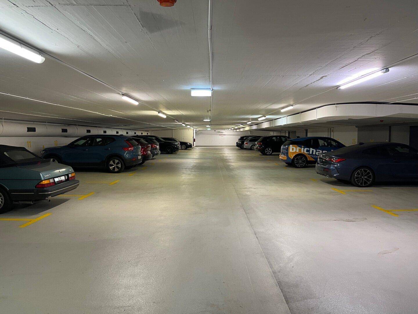 Weitläufige Tiefgarage mit mehreren geparkten Fahrzeugen und guter Beleuchtung durch Leuchtstoffröhren.