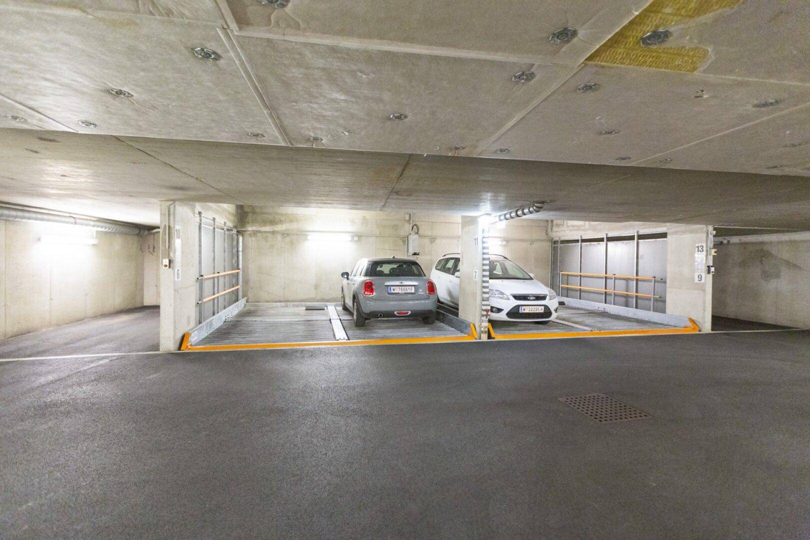 Zwei Fahrzeuge parken auf Auto-Lift-Systemen in einer sauberen und funktionalen Tiefgarage mit Betonwänden und -decken.