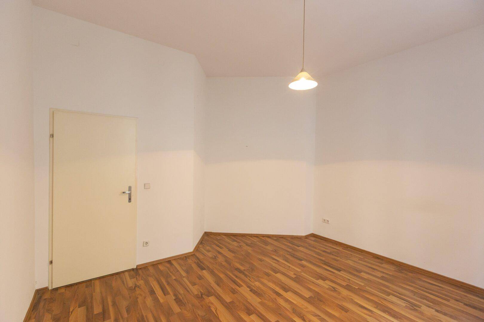 Leeres Zimmer mit Laminatboden und einer einfachen Tür, bereit zur individuellen Gestaltung.