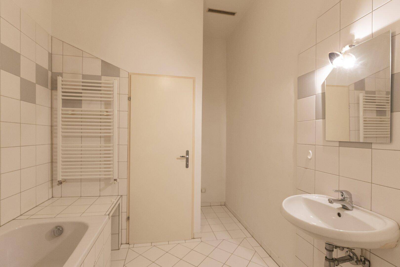 Badezimmer mit Badewanne, Waschbecken, beheiztem Handtuchhalter und weißen Fliesen.